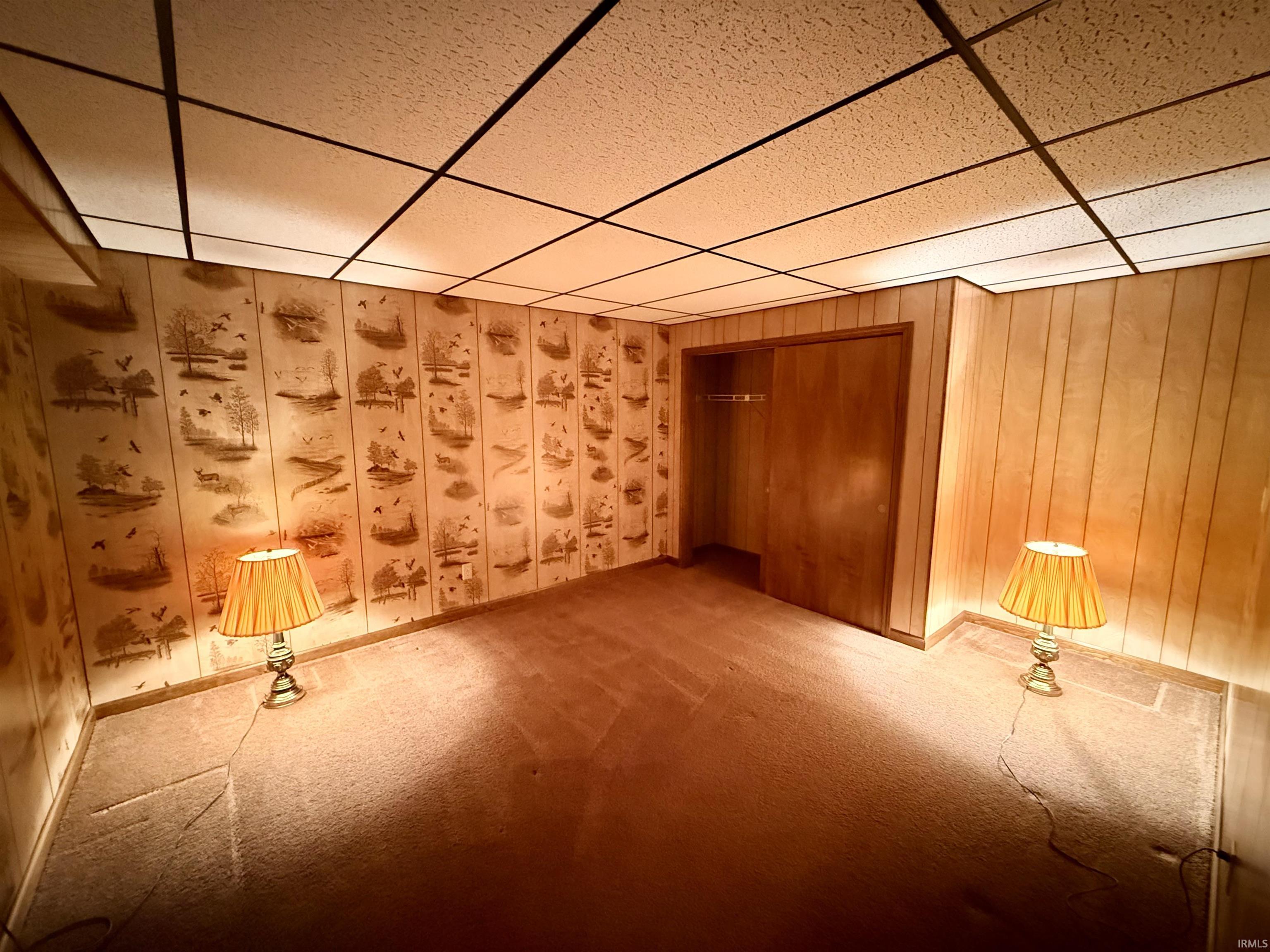 Unfurnished room with carpet floors, a drop ceiling, and wood walls
