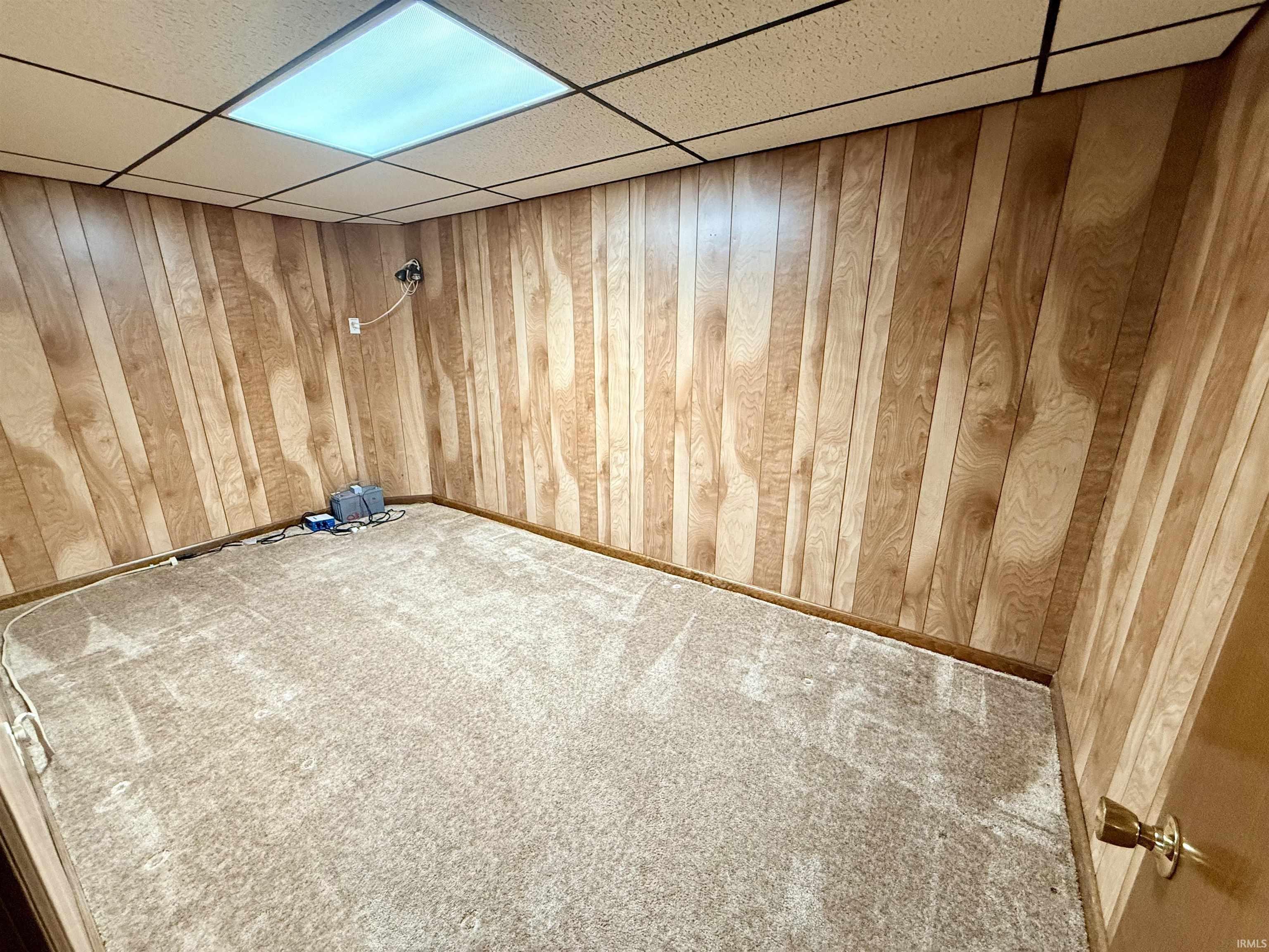 Carpeted spare room featuring a paneled ceiling and wood walls