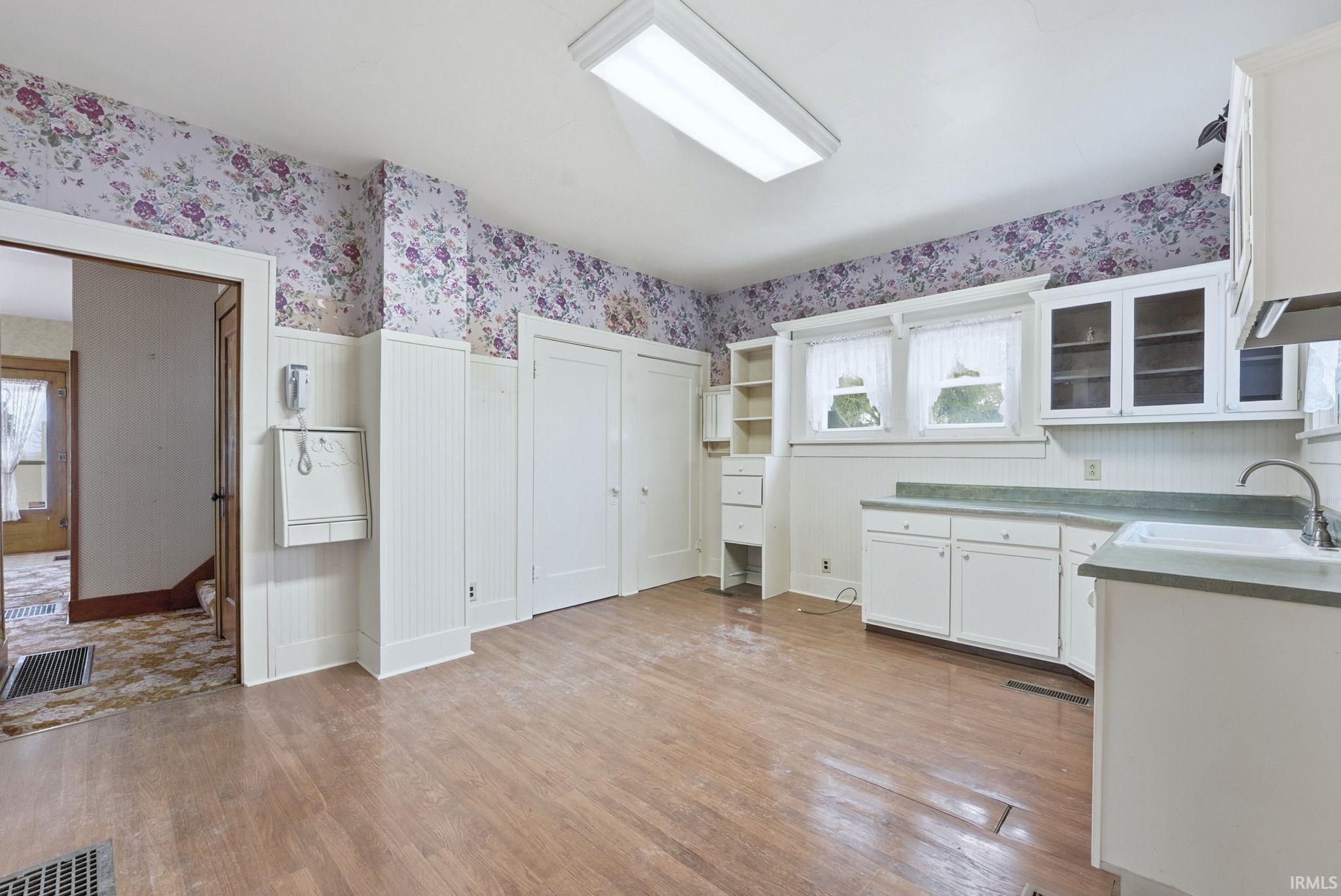 Kitchen with white cabinetry, wallpapered walls, light wood finished floors, and glass insert cabinets