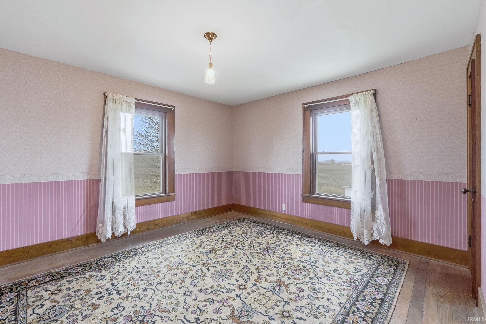 Empty room featuring wallpapered walls, wainscoting, and wood finished floors