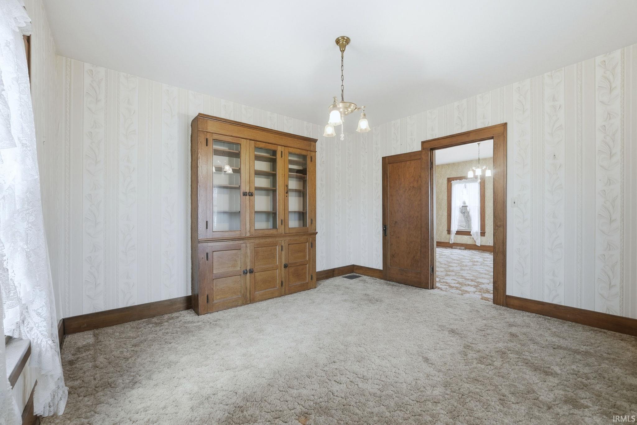 Carpeted spare room featuring a chandelier and wallpapered walls