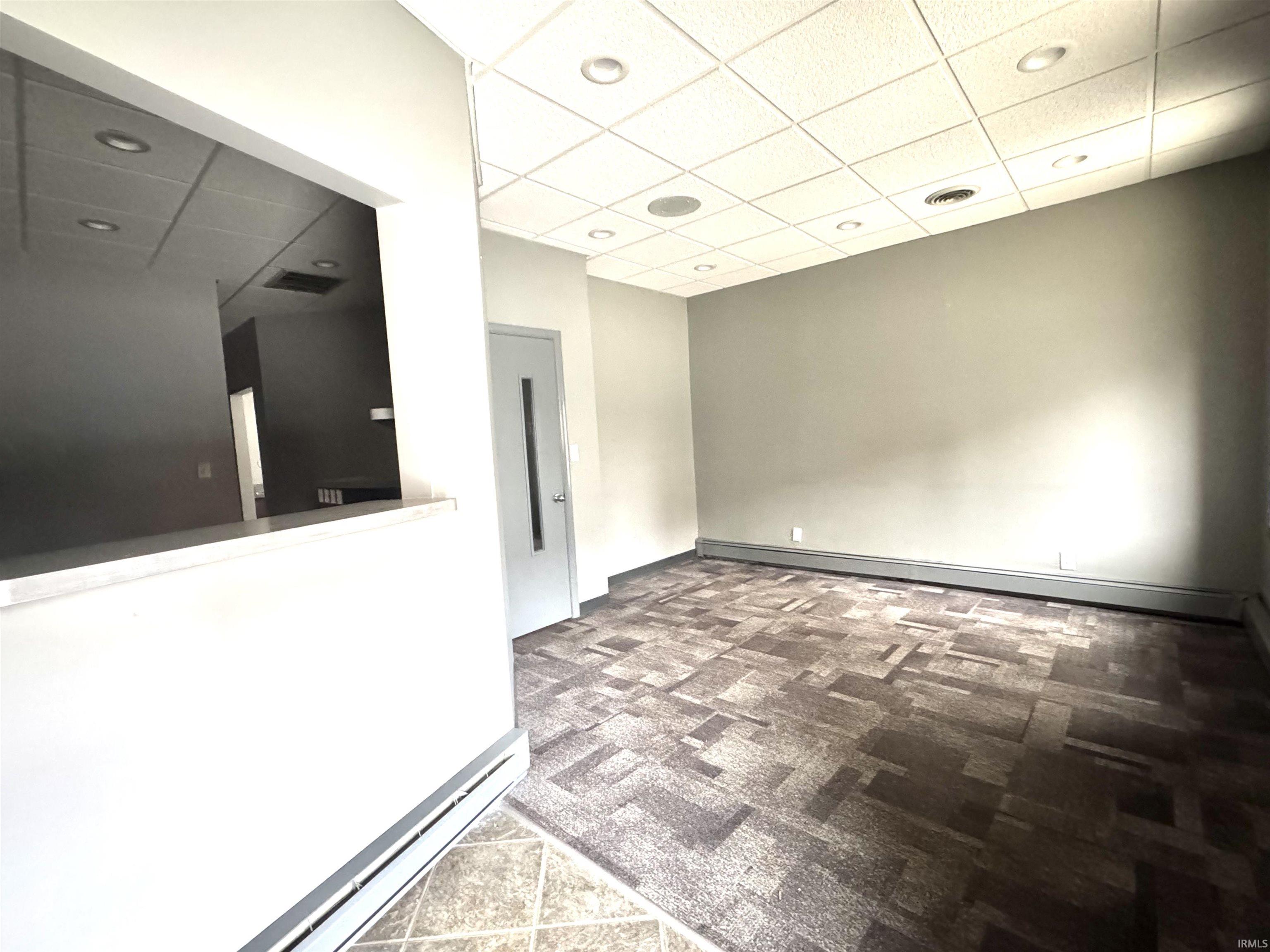 Carpeted empty room with a paneled ceiling, baseboard heating, and a baseboard radiator