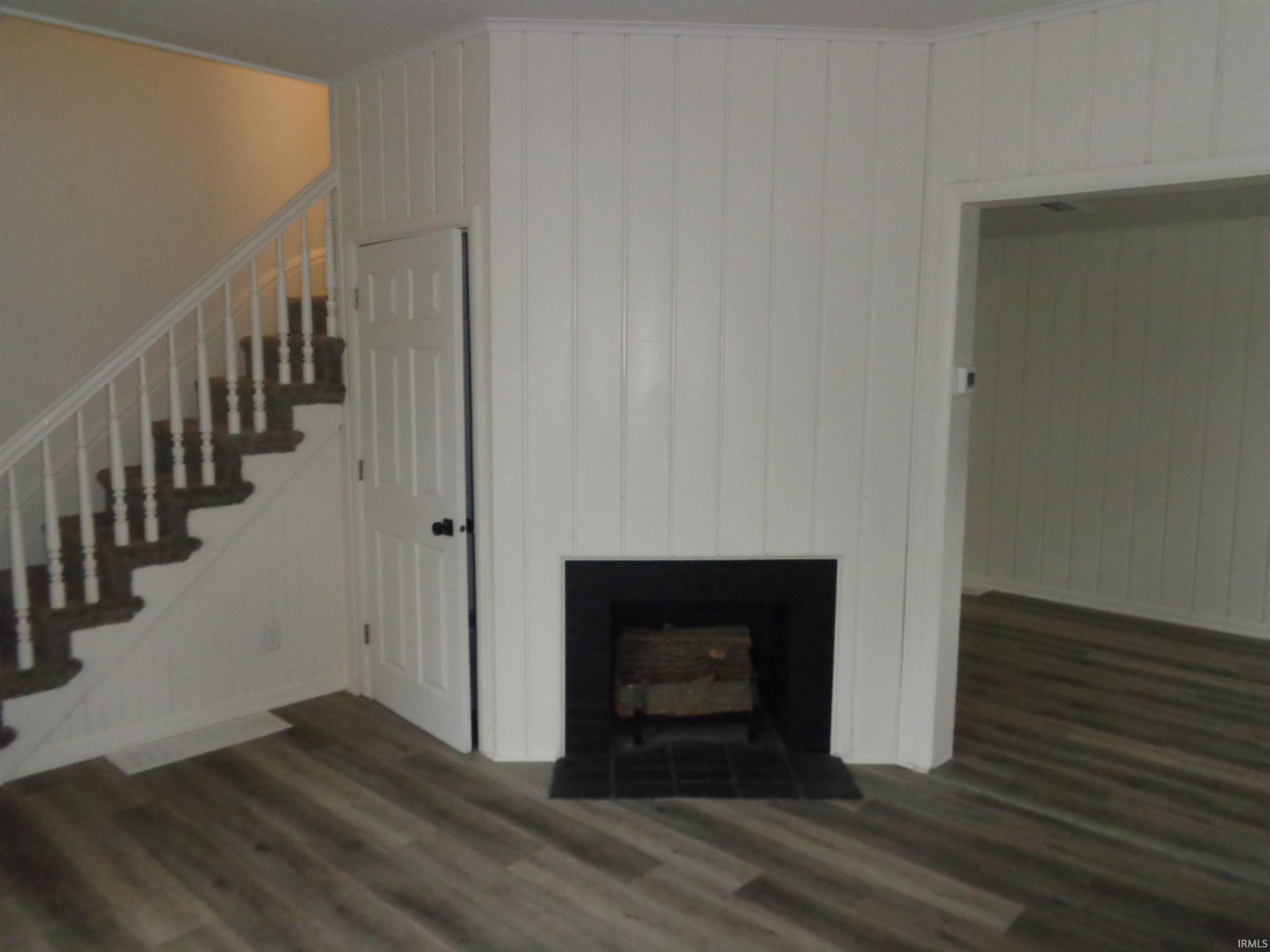 Unfurnished living room with dark wood-type flooring, stairs, a fireplace with flush hearth, and wood walls
