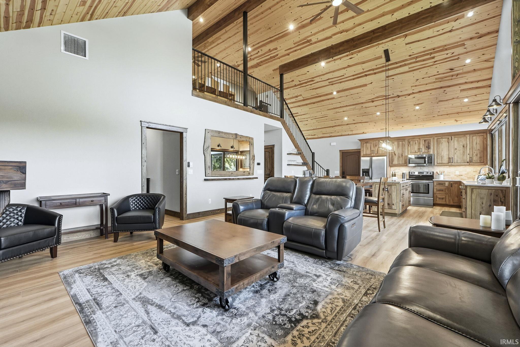 Living area with stairs, light wood finished floors, high vaulted ceiling, a wood ceiling with exposed beams, and ceiling fan