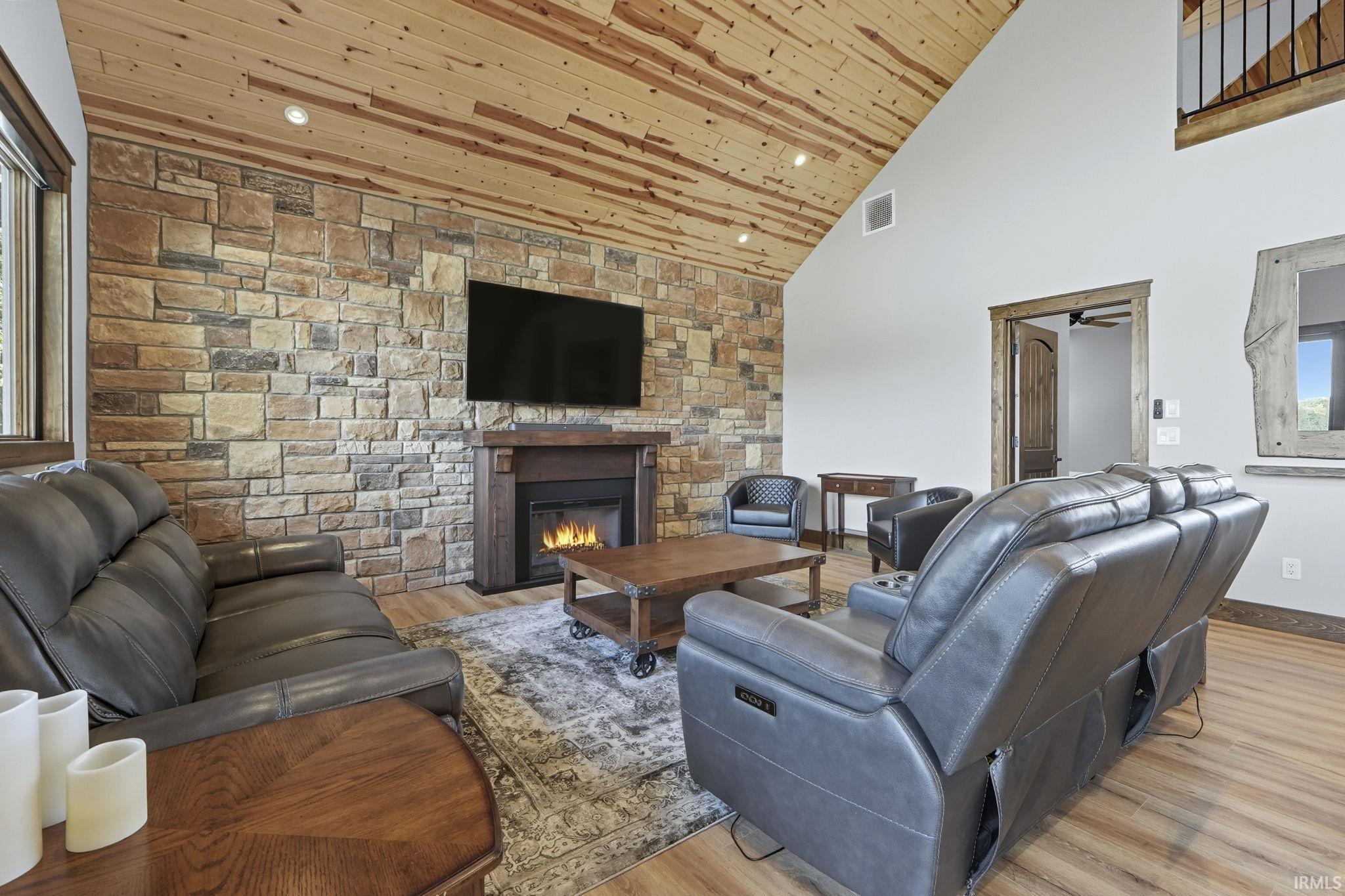 Living room with wood ceiling, high vaulted ceiling, a stone fireplace, light wood finished floors, and recessed lighting