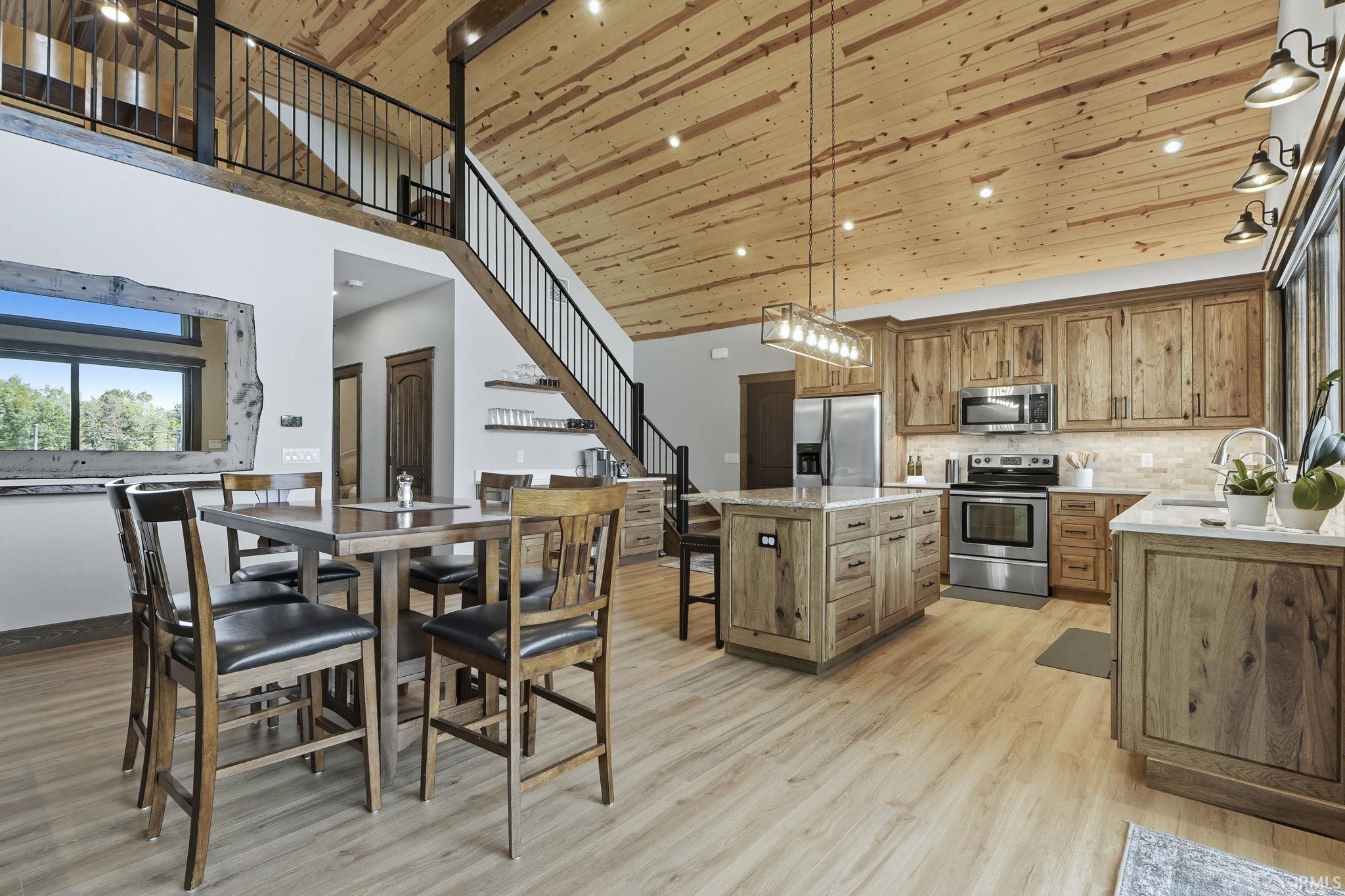 Kitchen with pendant lighting, a kitchen island, stainless steel appliances, light stone counters, and light wood finished floors