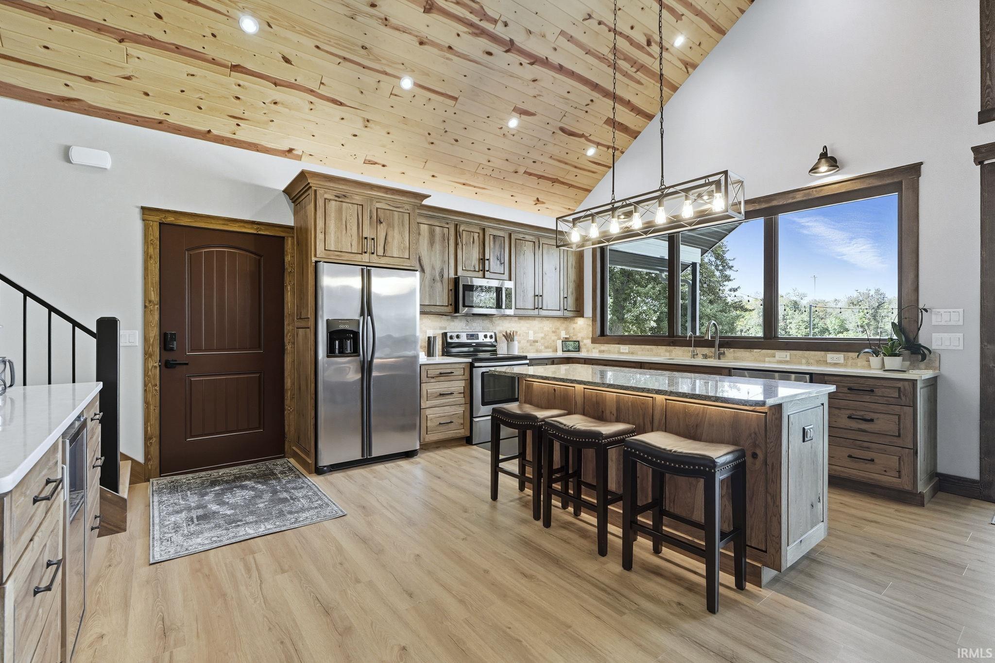 Kitchen with a breakfast bar, stainless steel appliances, a center island, wooden ceiling, and high vaulted ceiling