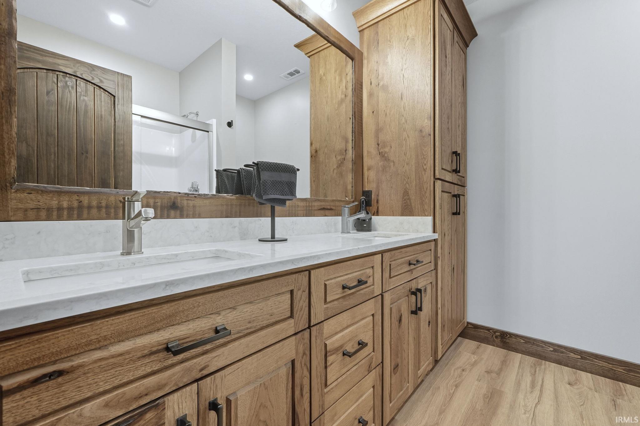 Bathroom featuring double vanity, a shower stall, and light wood-style floors