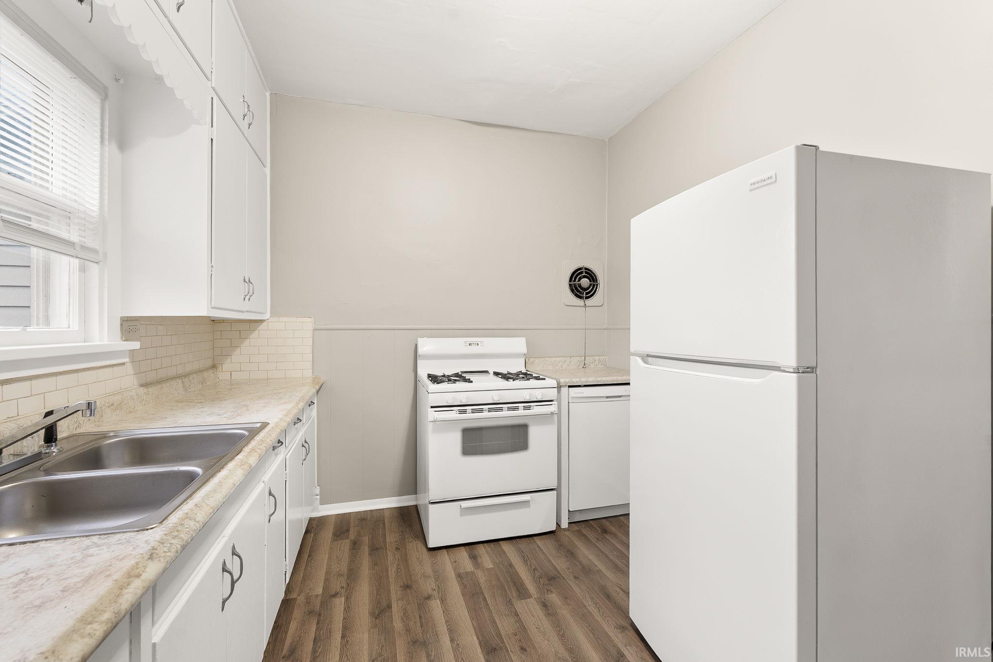 Kitchen featuring white appliances, white cabinetry, light countertops, and dark wood-style flooring