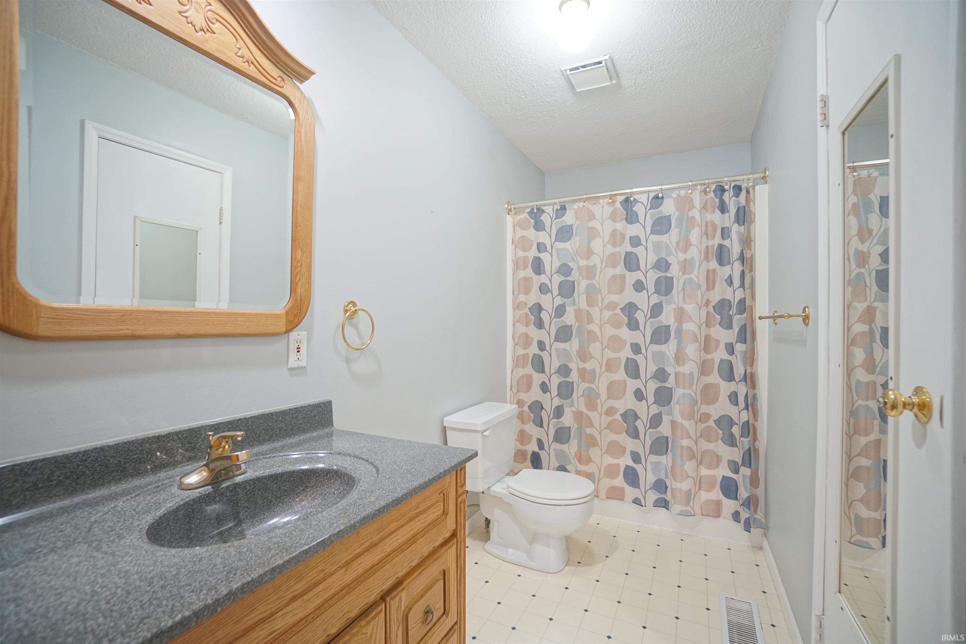 Full bath with vanity, a shower with shower curtain, a textured ceiling, and light floors