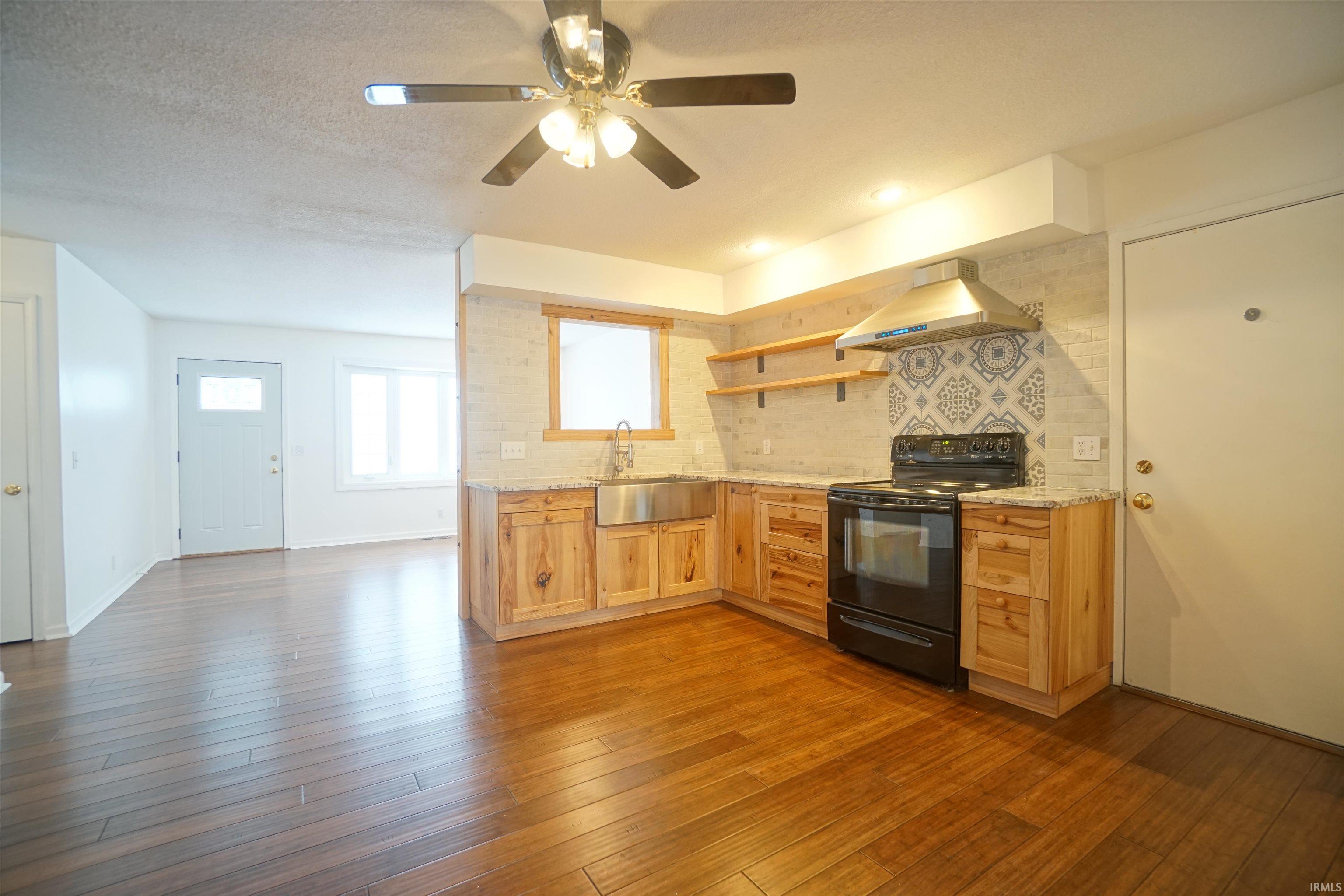 Kitchen featuring black range with electric stovetop, open shelves, island exhaust hood, dark wood finished floors, and backsplash