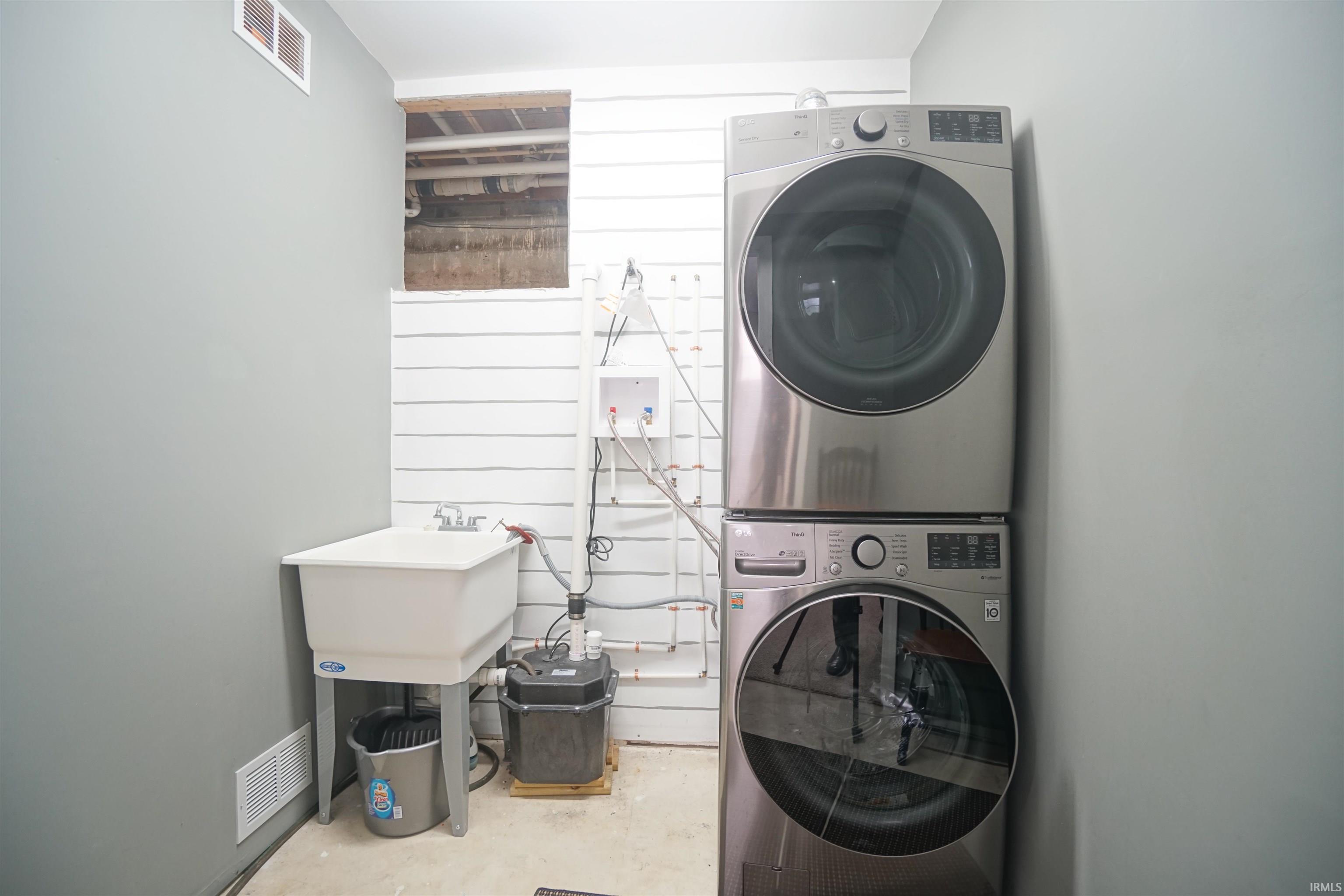 Laundry area featuring stacked washer and clothes dryer, concrete floors, and wood walls