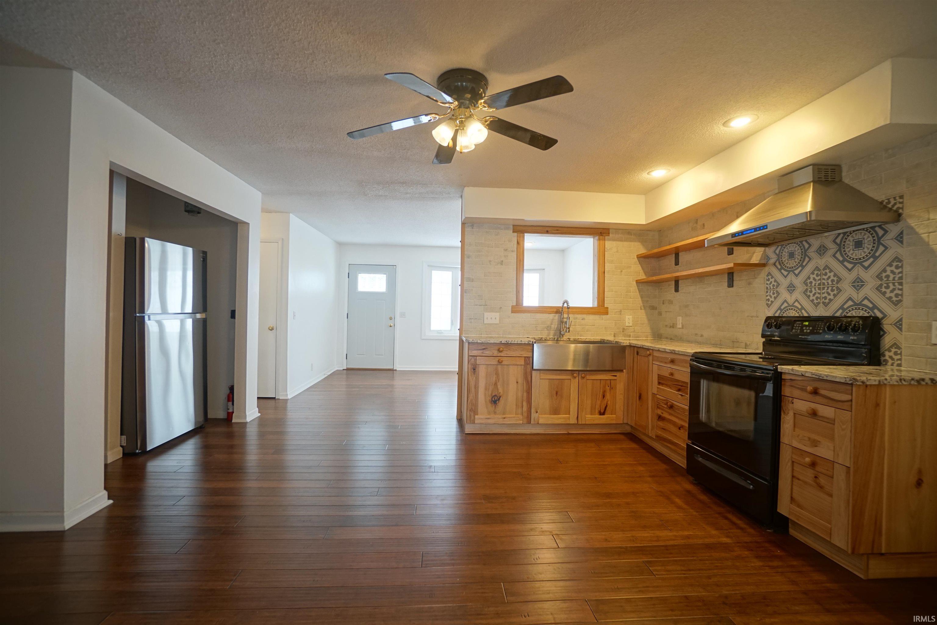 Kitchen featuring black range with electric stovetop, open shelves, island range hood, freestanding refrigerator, and light stone counters