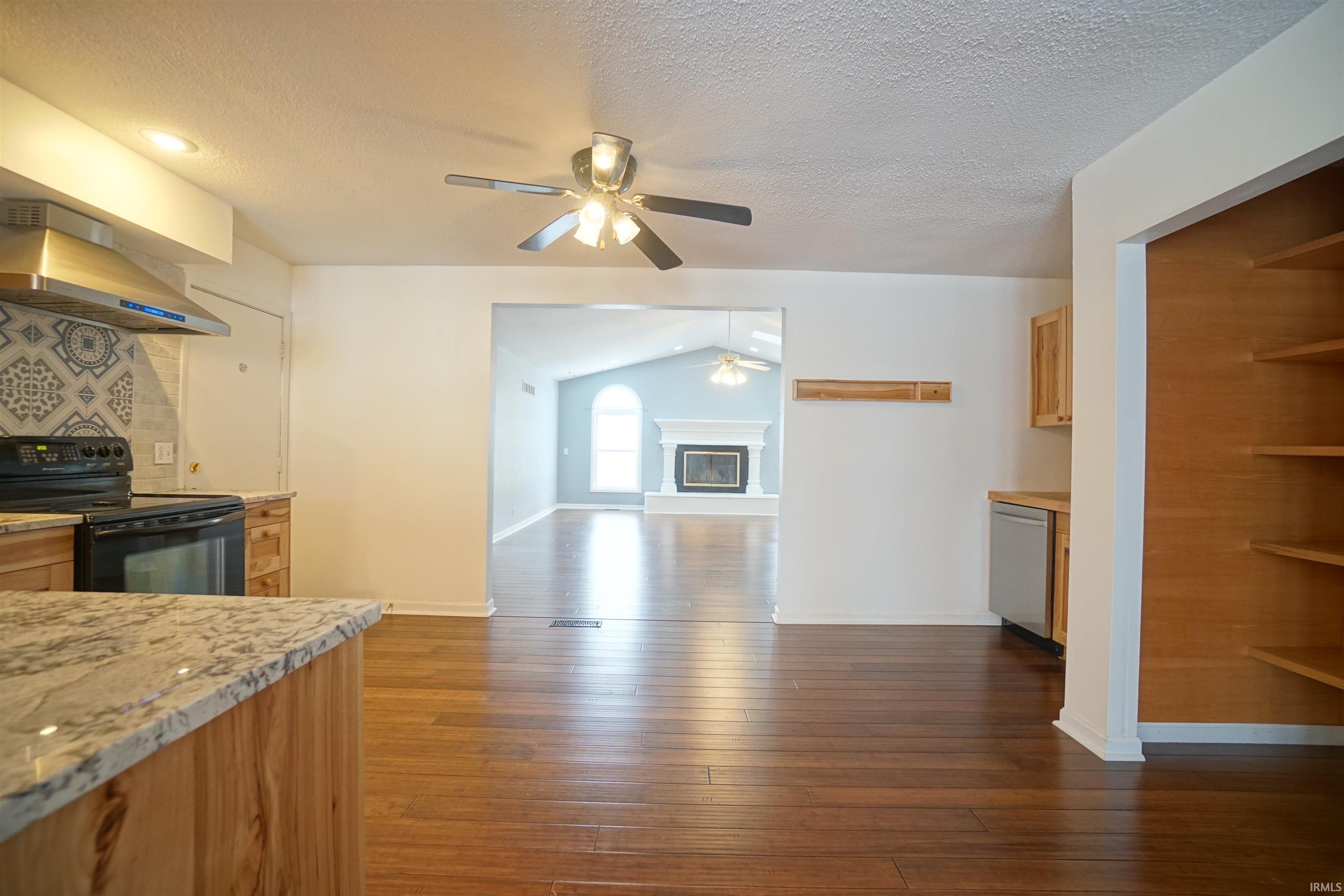 Kitchen featuring black electric range, extractor fan, a textured ceiling, a glass covered fireplace, and lofted ceiling
