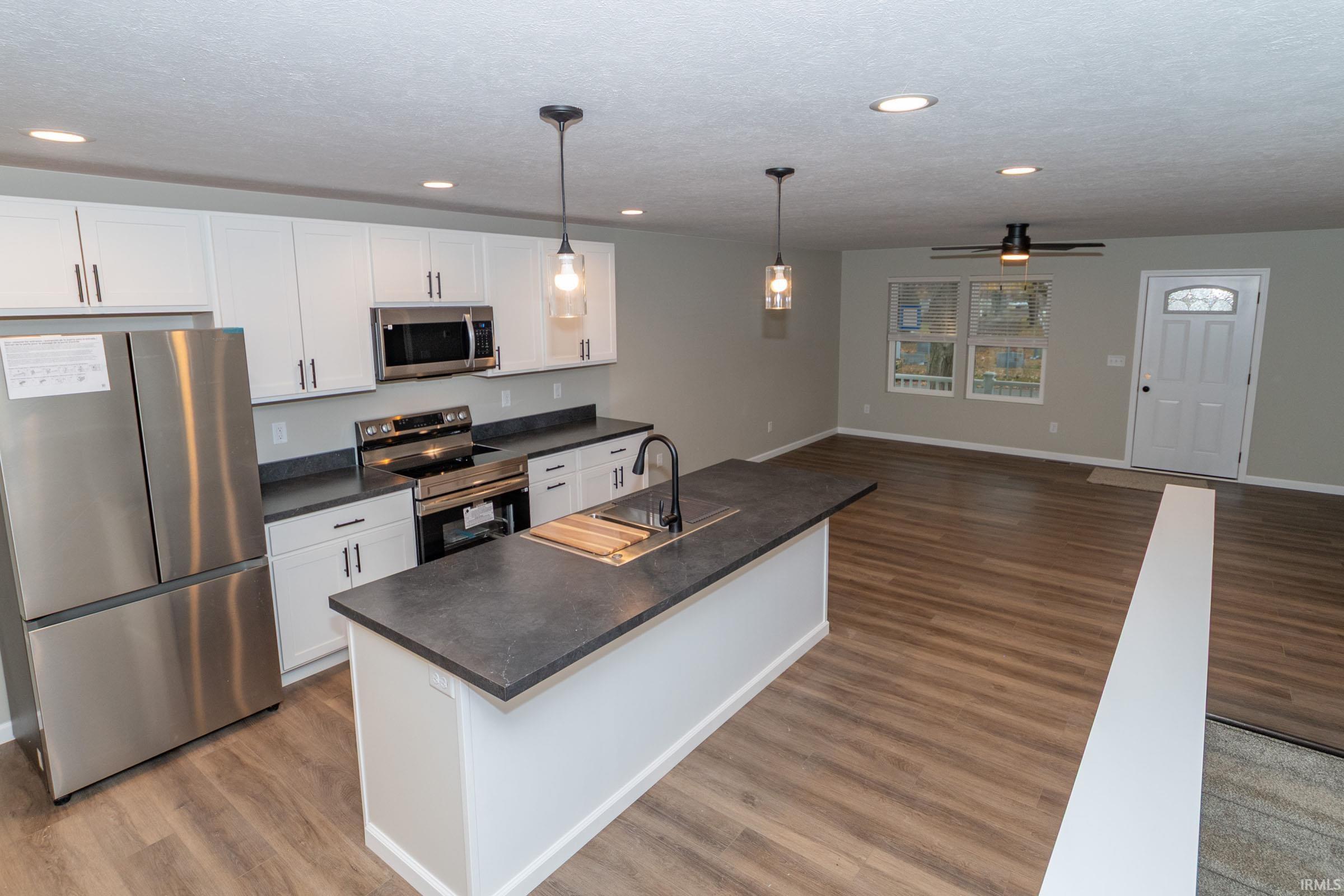 Kitchen with appliances with stainless steel finishes, open floor plan, white cabinets, pendant lighting, and dark countertops