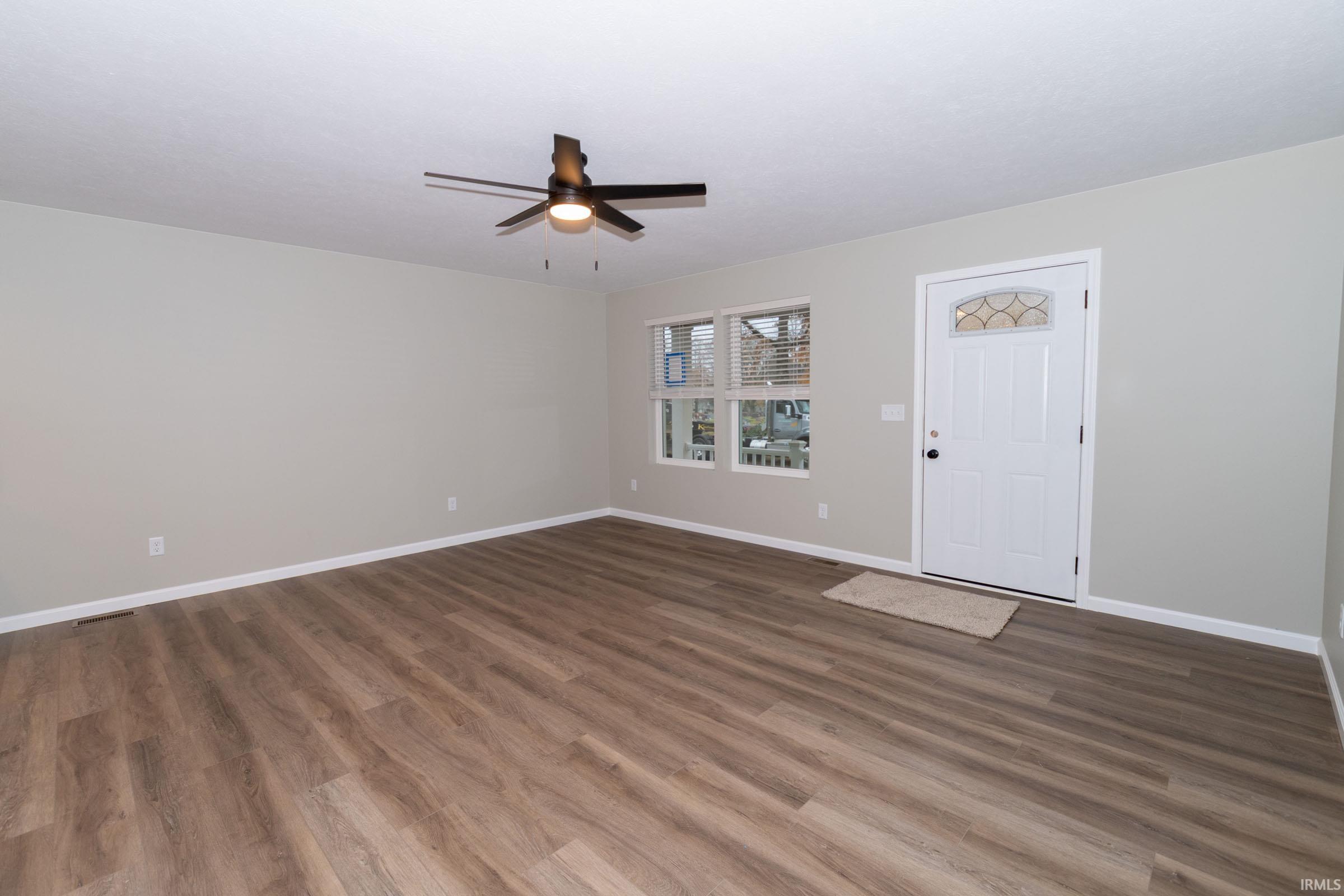 Unfurnished living room featuring dark wood-style flooring and ceiling fan