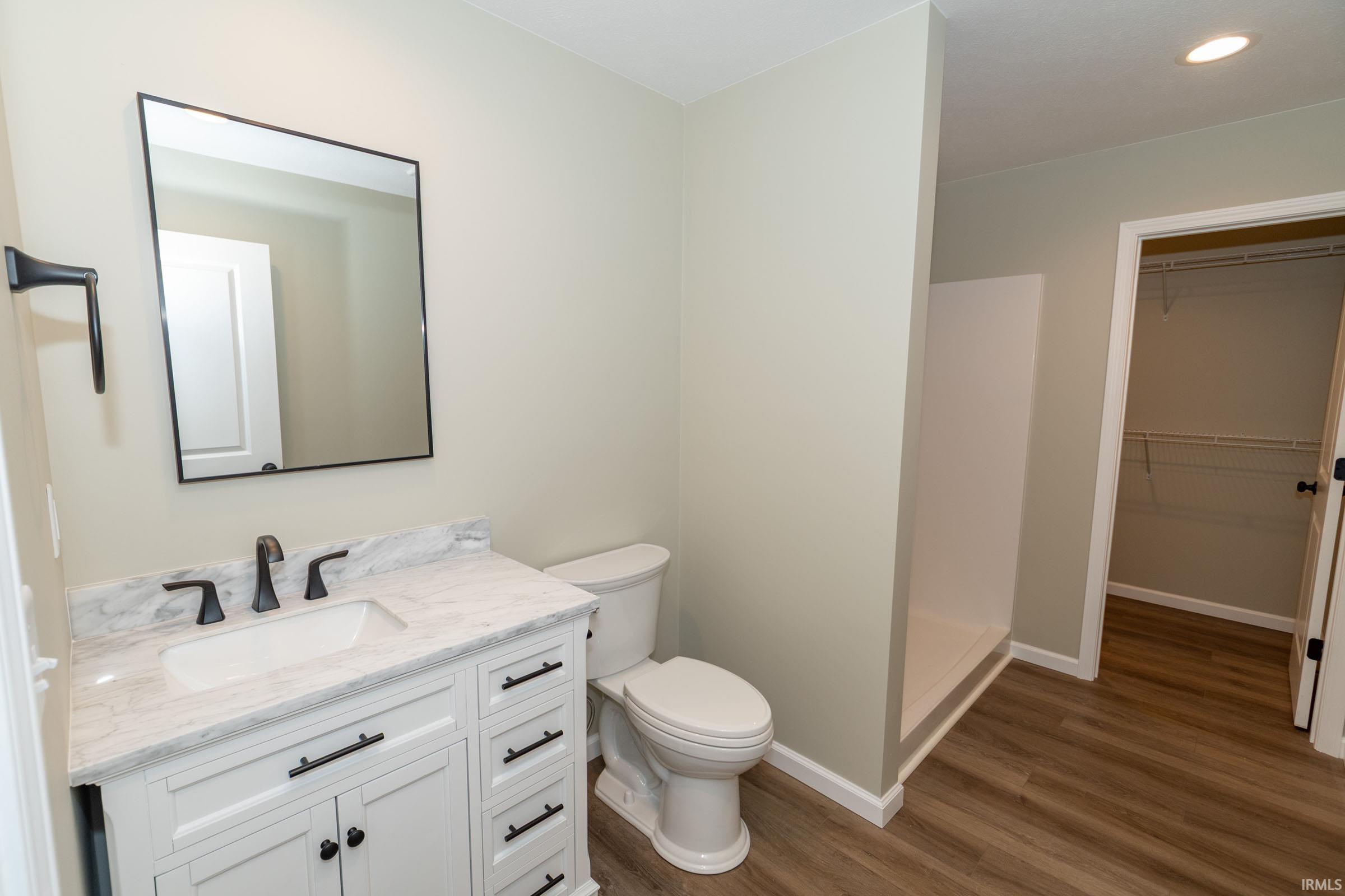 Bathroom with a spacious closet, vanity, wood finished floors, recessed lighting, and a stall shower