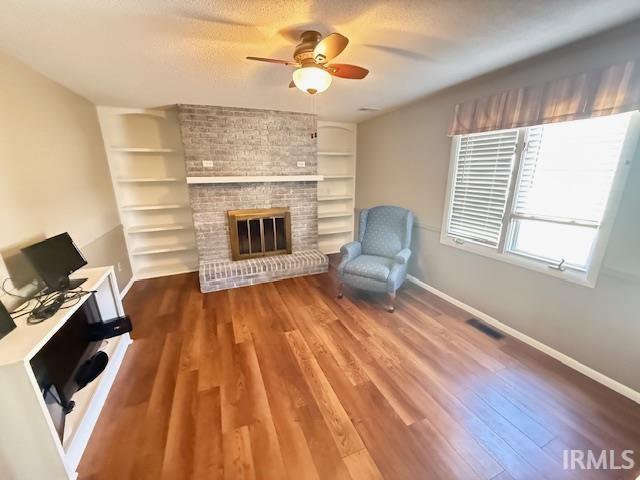 Unfurnished room with dark wood-type flooring, a ceiling fan, built in features, a brick fireplace, and a textured ceiling