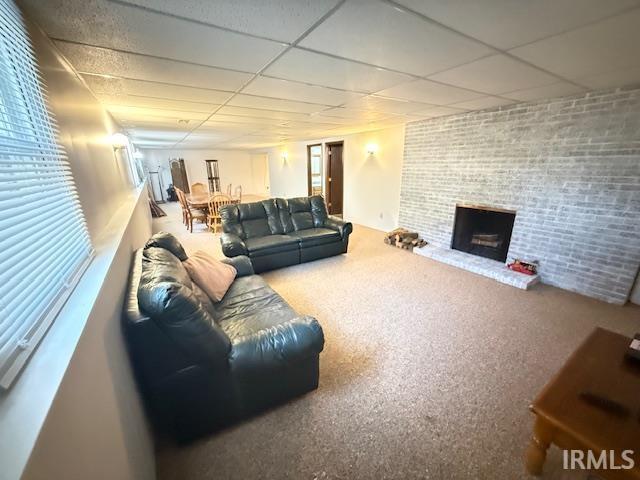 Carpeted living area with a paneled ceiling, brick wall, and a brick fireplace
