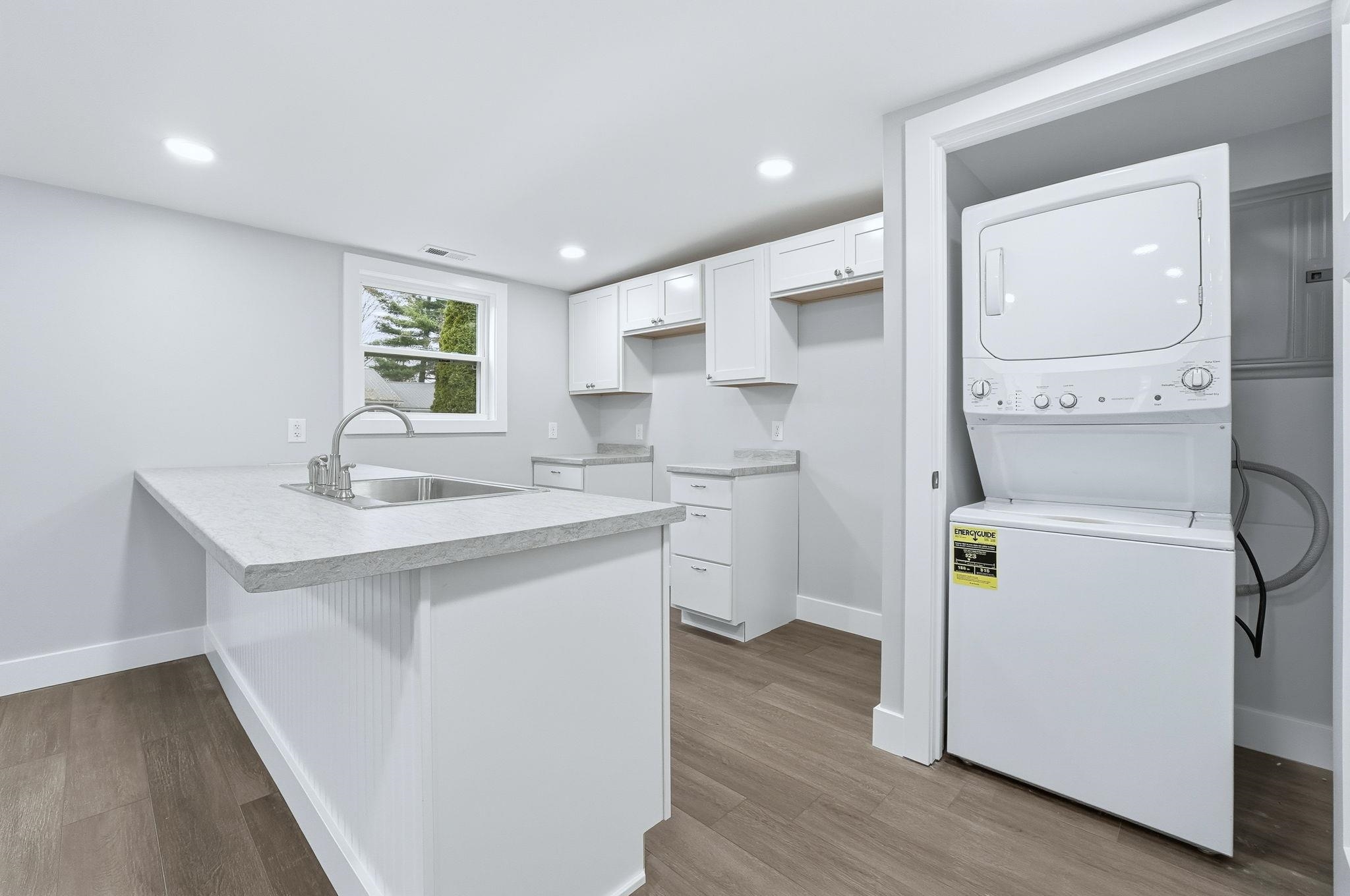 Kitchen with light countertops, white cabinets, a peninsula, stacked washing machine and dryer, and light wood-style flooring