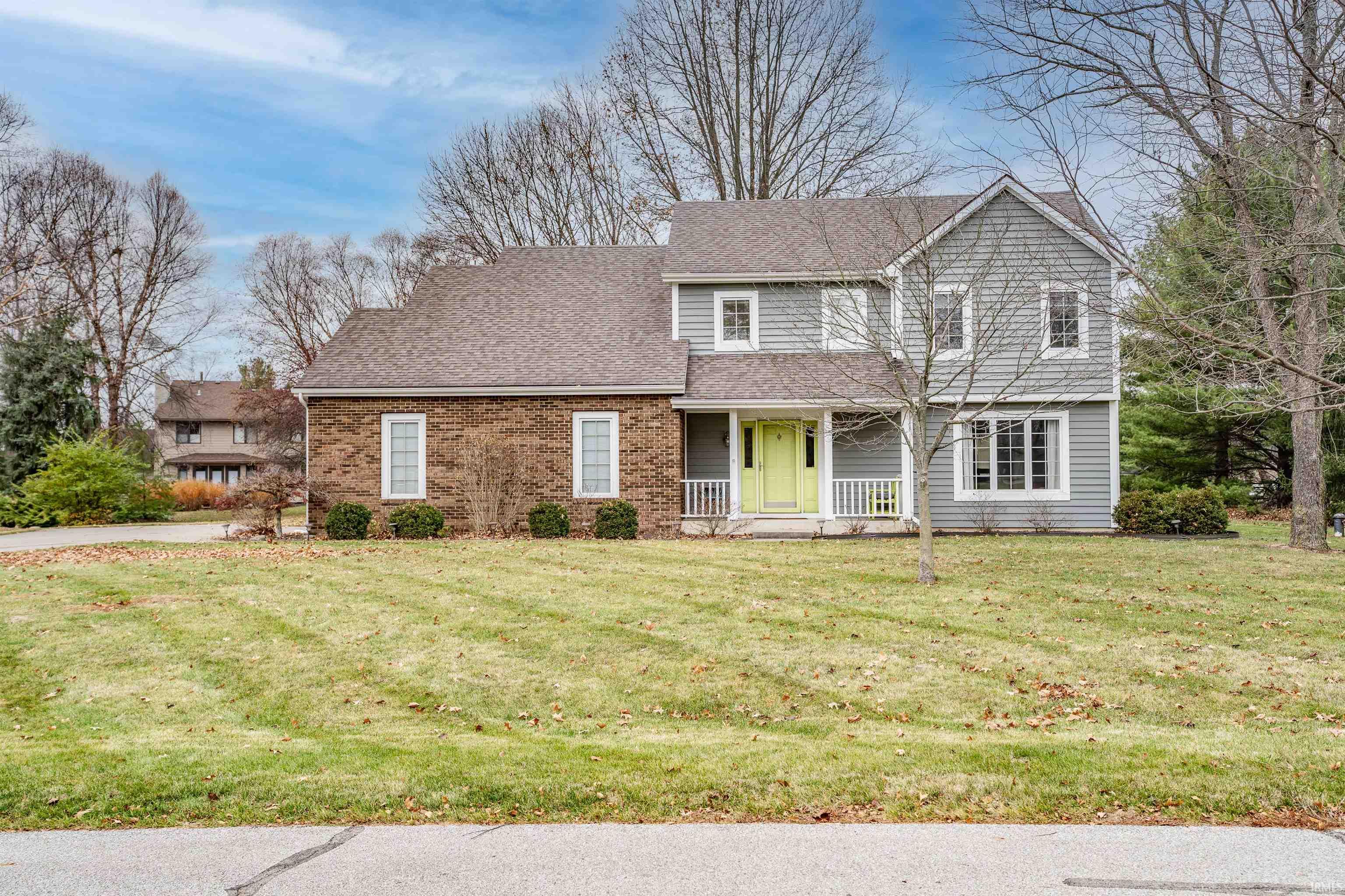 View of front of house with a porch, a front lawn, a shingled roof, and brick siding