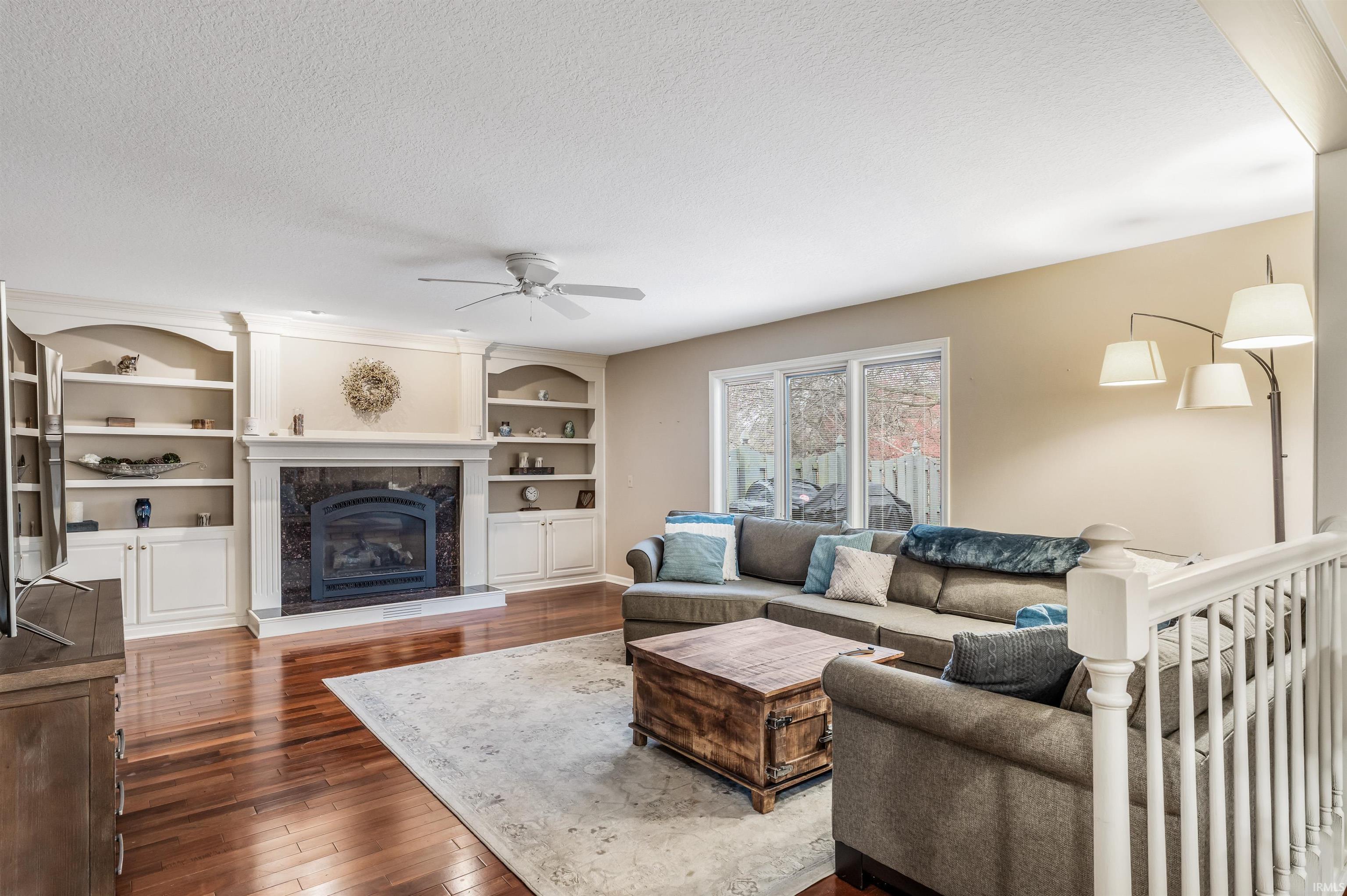 Living room featuring a fireplace, hardwood / wood-style flooring, a textured ceiling, a ceiling fan, and built in features