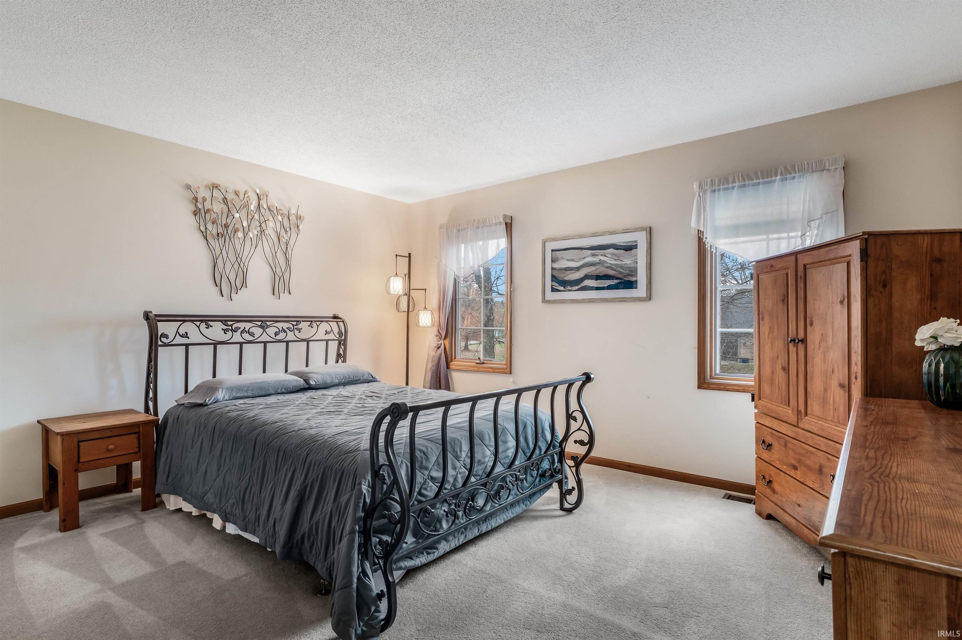 Bedroom with multiple windows, a textured ceiling, and light carpet