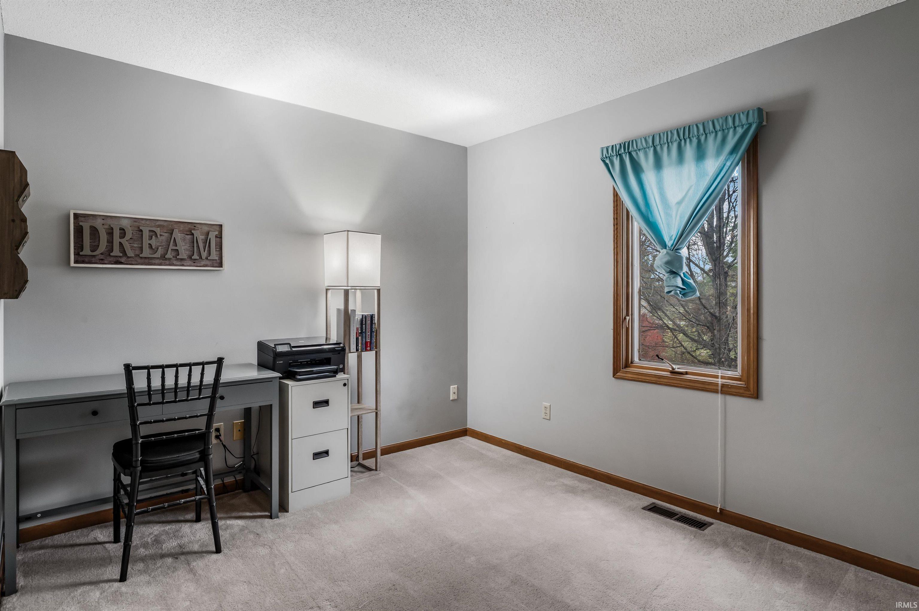 Home office with a textured ceiling and light colored carpet