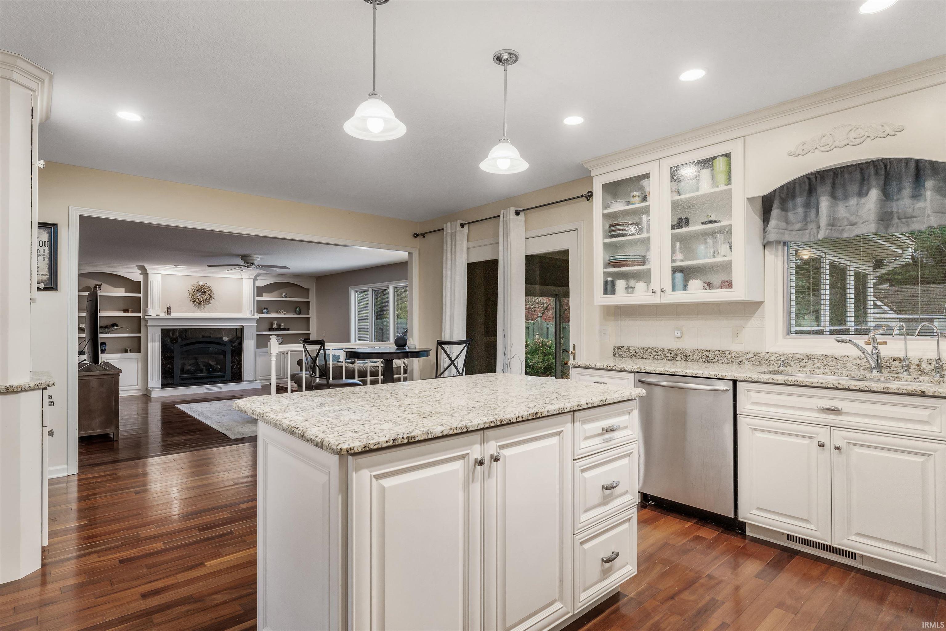 Kitchen with a fireplace with raised hearth, dishwasher, a kitchen island, hanging light fixtures, and light stone countertops