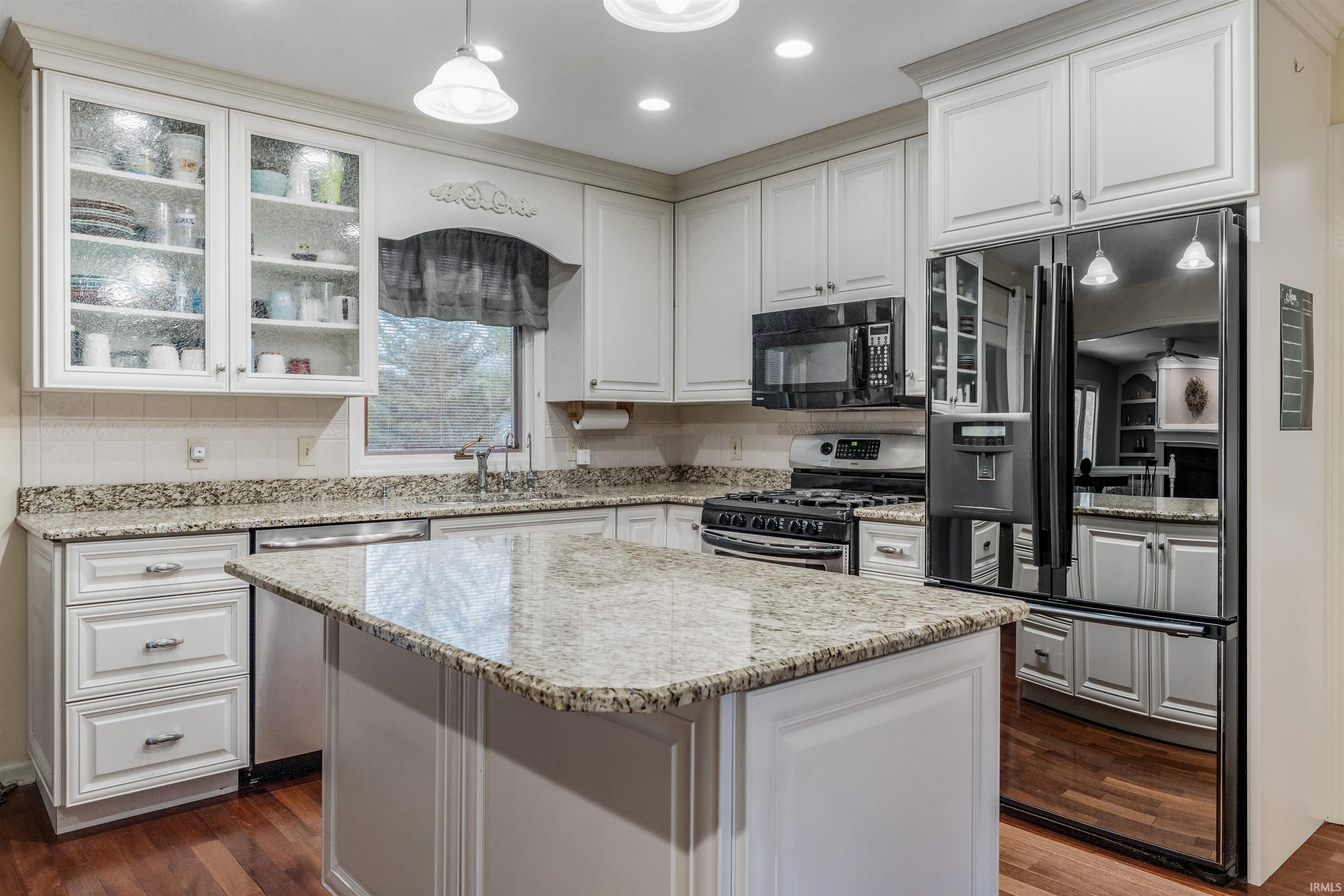 Kitchen with stainless steel appliances, glass insert cabinets, light stone countertops, white cabinets, and decorative light fixtures