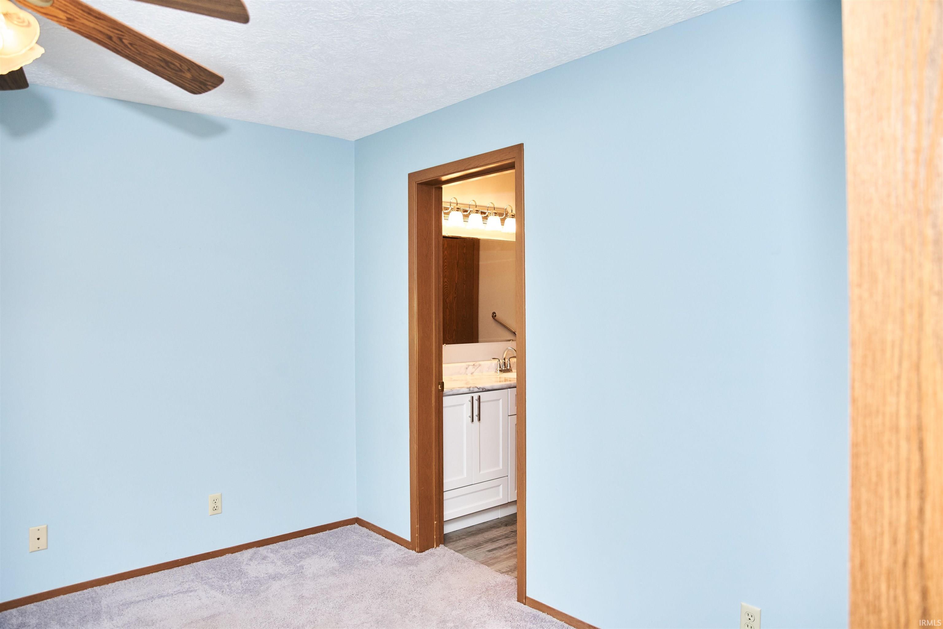 Unfurnished bedroom with a textured ceiling, carpet floors, connected bathroom, and ceiling fan