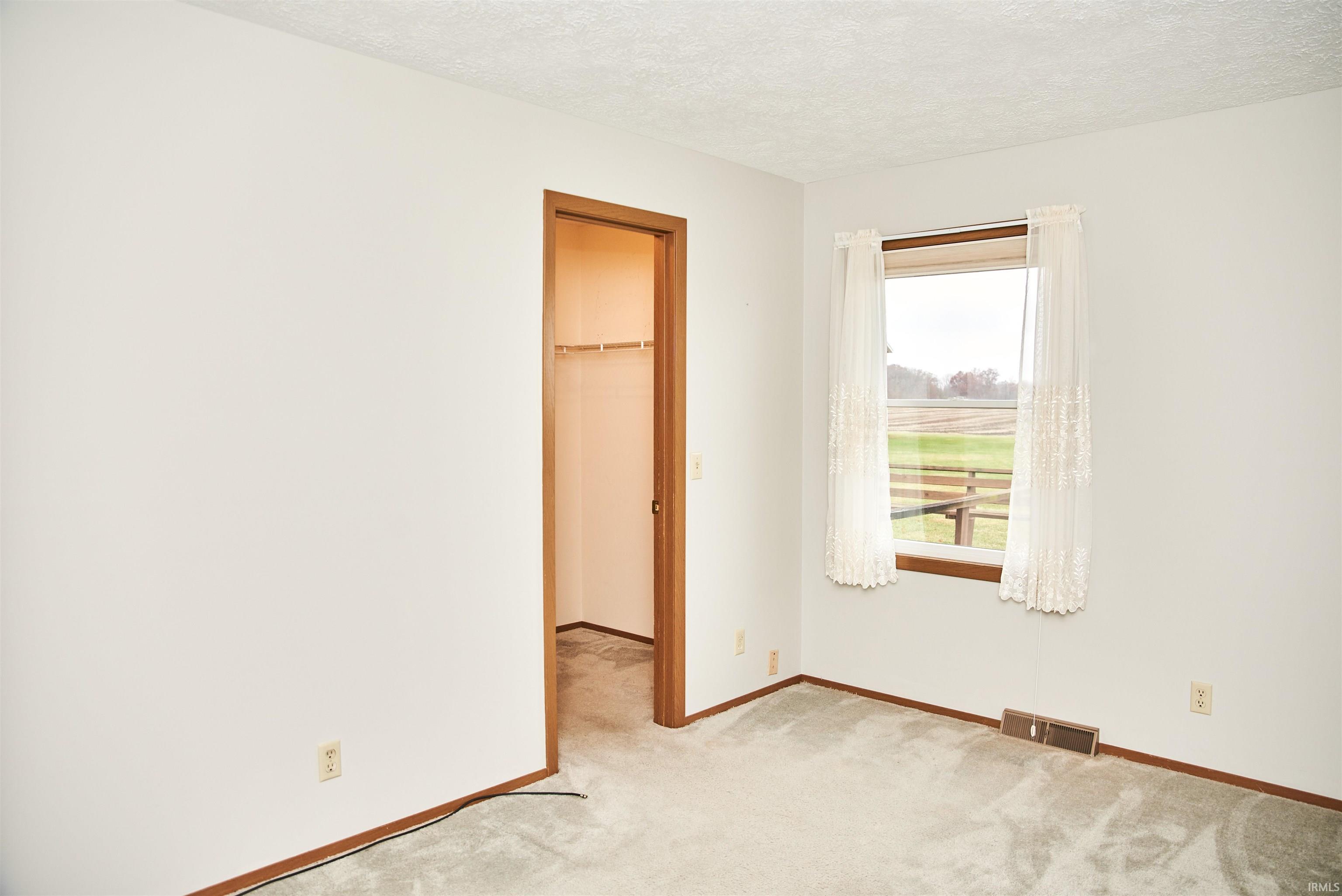 Unfurnished bedroom with a spacious closet, light colored carpet, and a textured ceiling