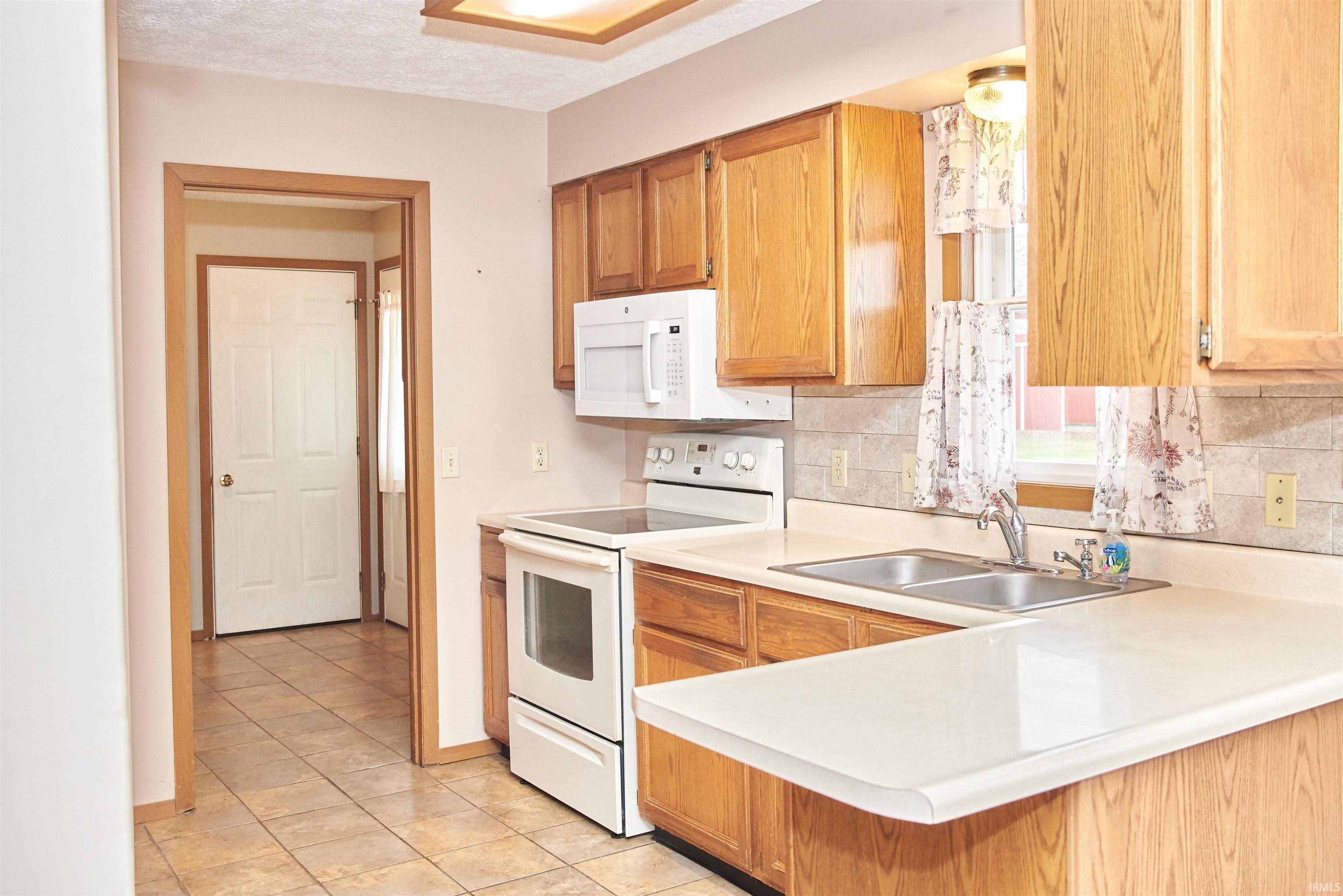 Kitchen with white appliances, light countertops, tasteful backsplash, light tile patterned flooring, and a peninsula