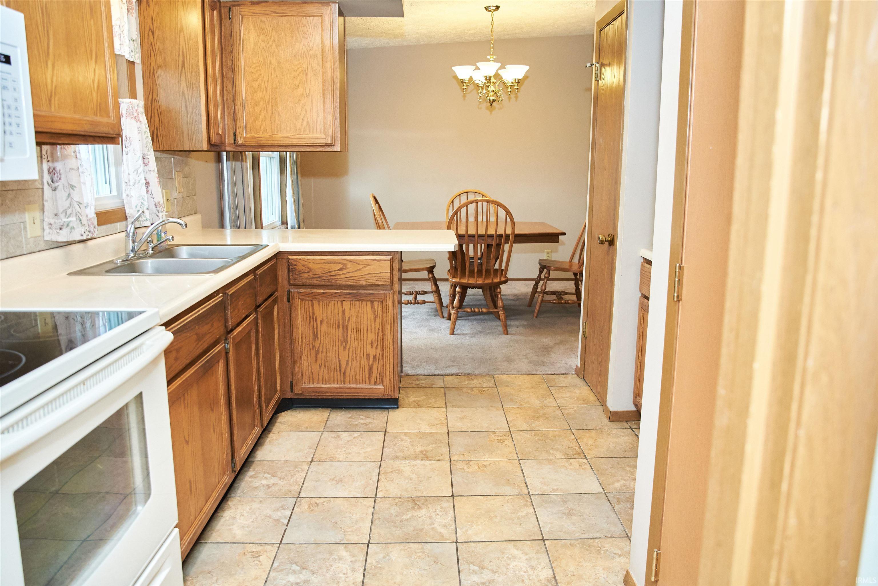 Kitchen with white appliances, light countertops, pendant lighting, brown cabinetry, and a peninsula
