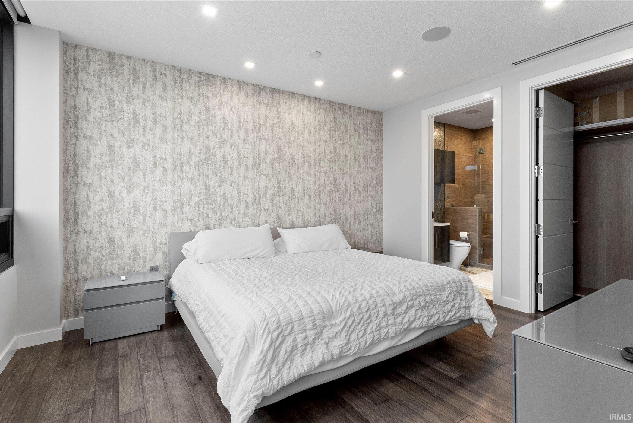 Bedroom with wallpapered walls, dark wood finished floors, recessed lighting, and an accent wall