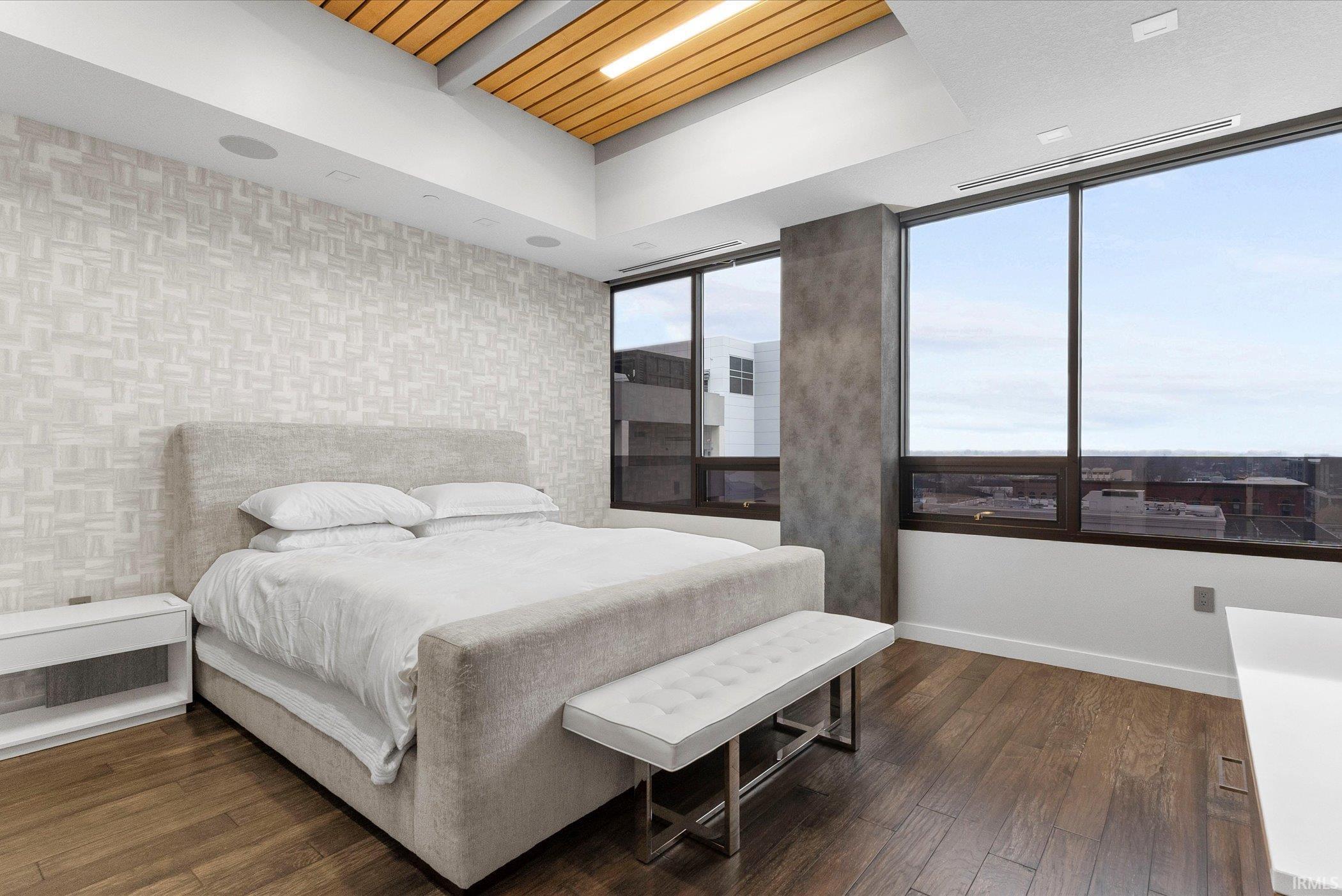 Bedroom with an accent wall, wallpapered walls, and dark wood-type flooring