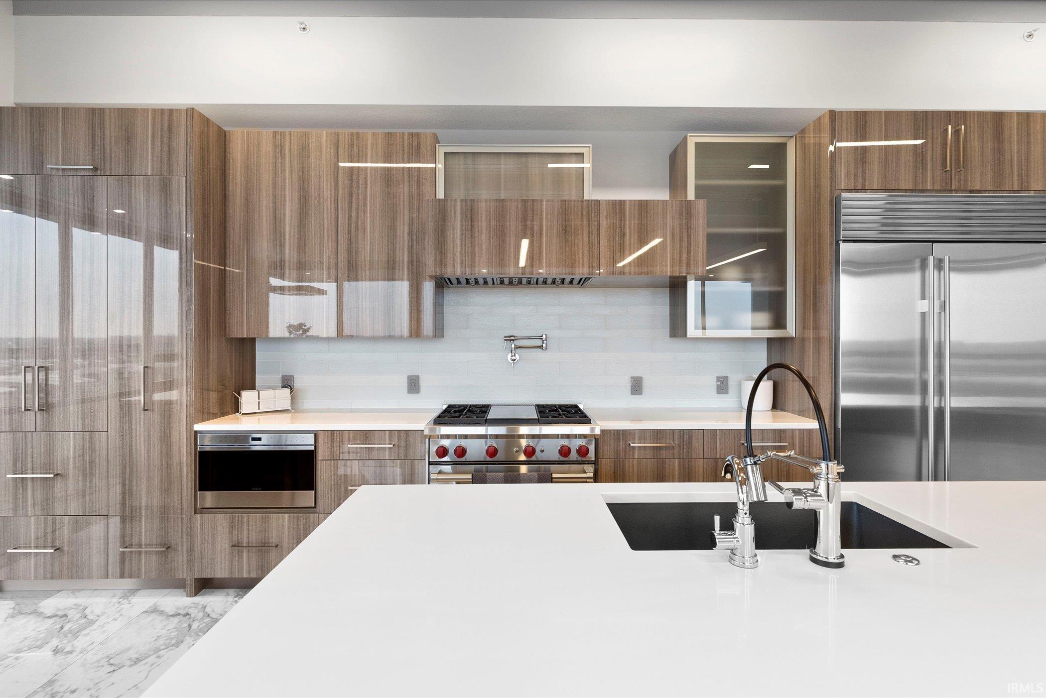 Kitchen with high end appliances, modern cabinets, brown cabinets, tasteful backsplash, and light stone countertops