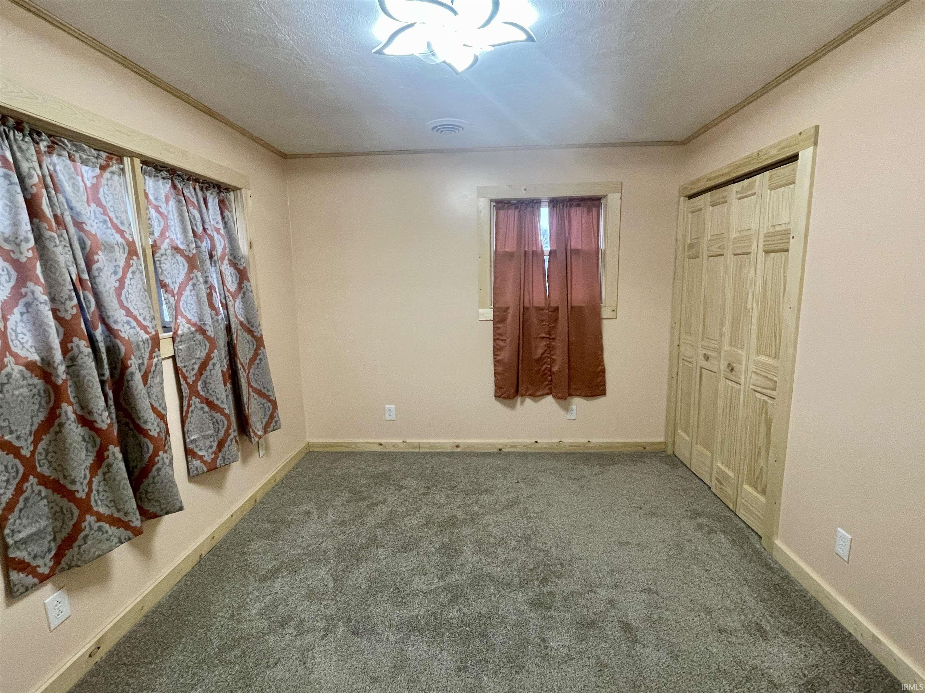 Unfurnished bedroom with carpet floors, crown molding, a textured ceiling, and a closet