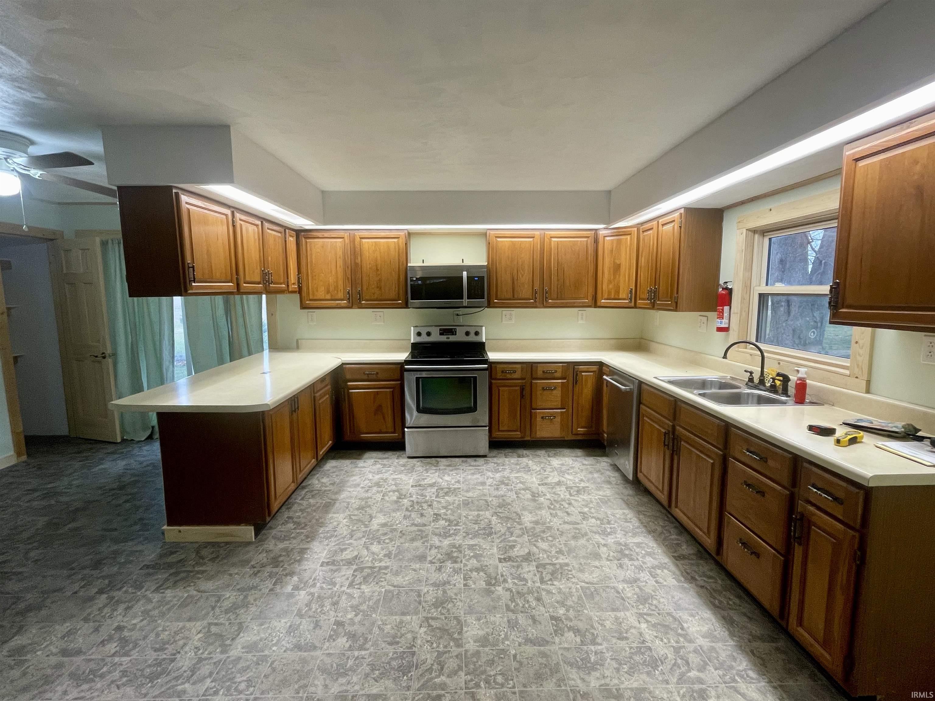 Kitchen featuring light countertops, appliances with stainless steel finishes, brown cabinets, and a peninsula