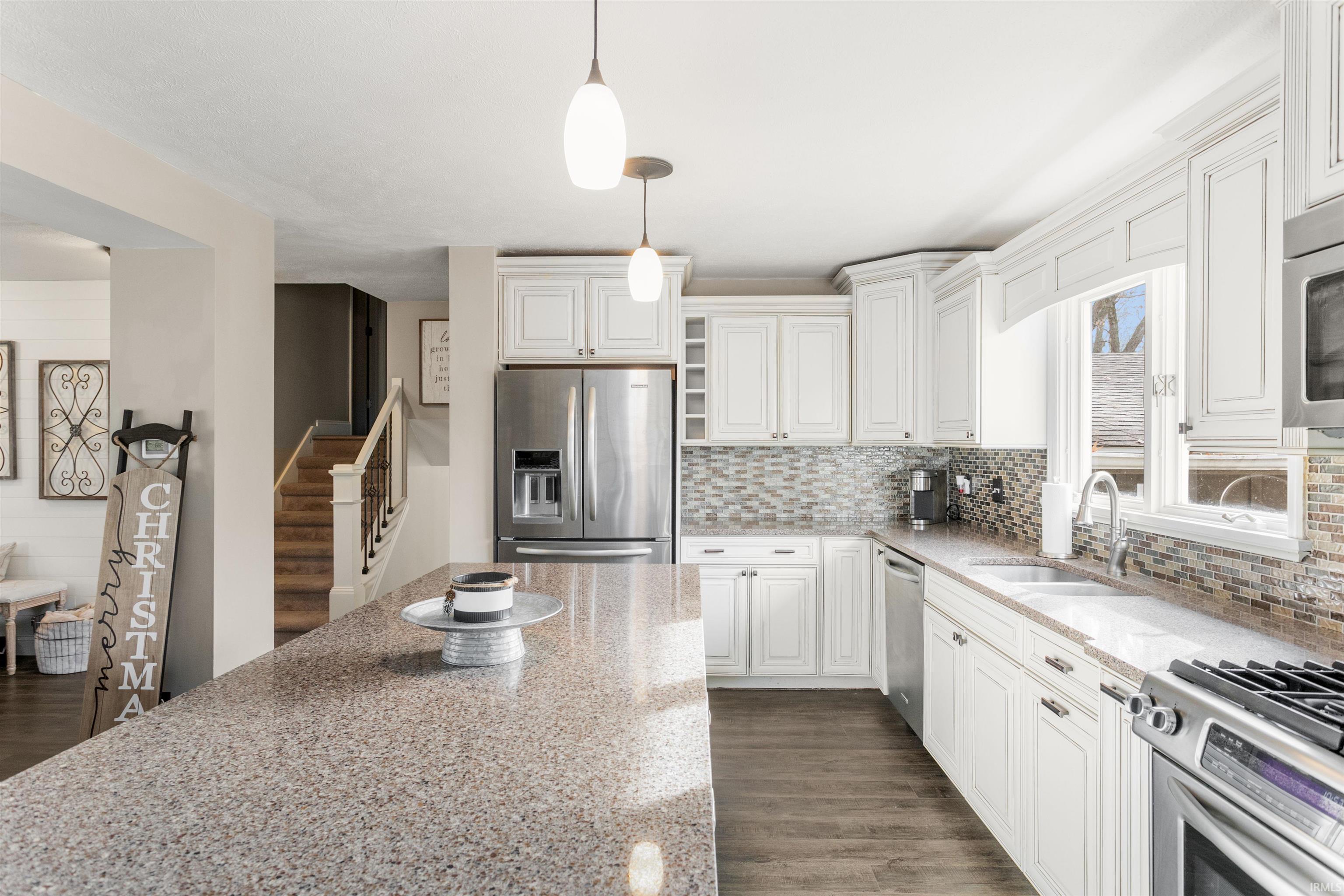 Kitchen featuring appliances with stainless steel finishes, decorative light fixtures, light stone counters, dark wood-style flooring, and white cabinetry