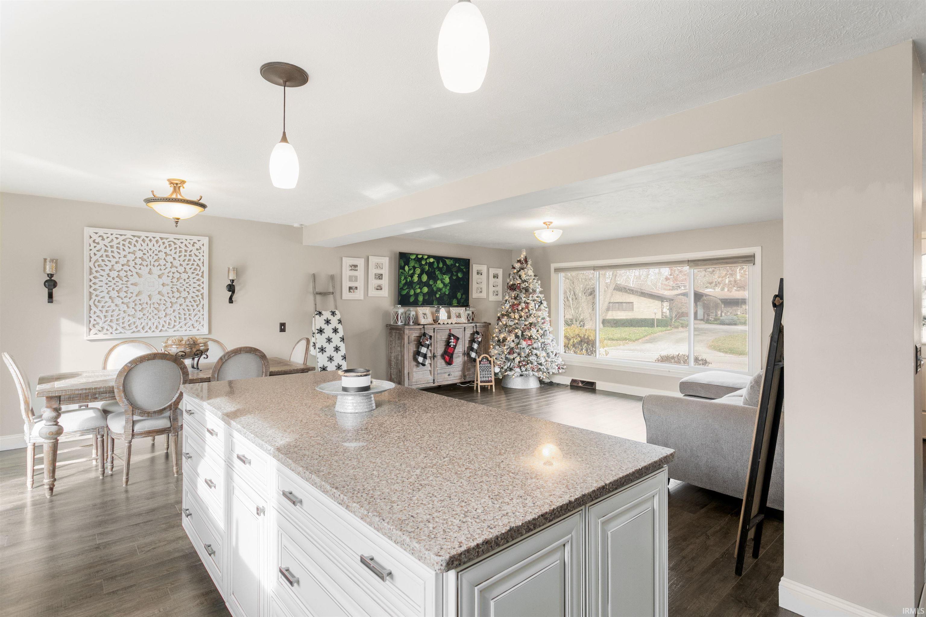 Kitchen featuring open floor plan, white cabinets, hanging light fixtures, light stone countertops, and a kitchen island