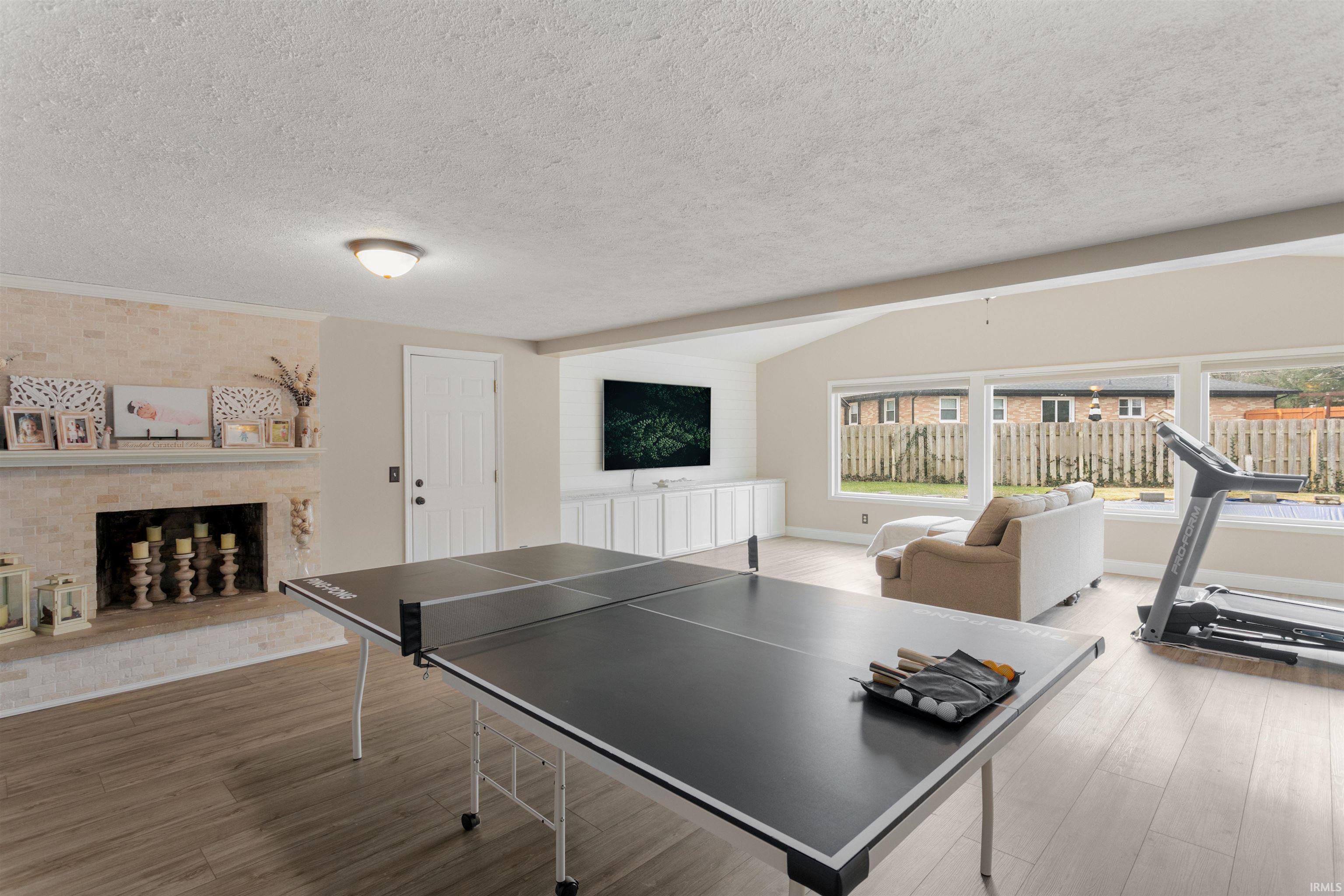 Playroom featuring a brick fireplace, light wood-type flooring, a textured ceiling, and beamed ceiling