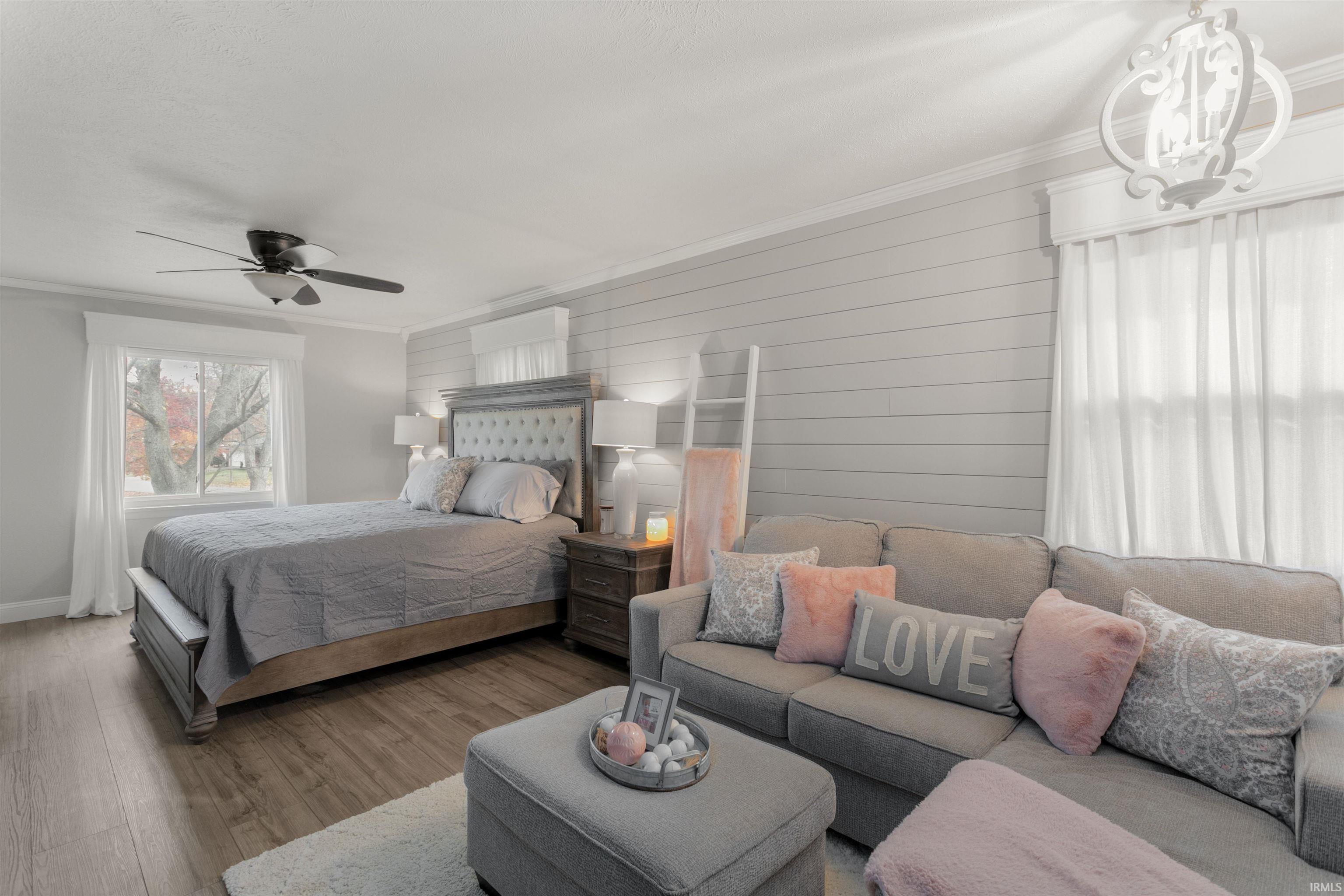 Bedroom with multiple windows, crown molding, wood finished floors, wooden walls, and a ceiling fan