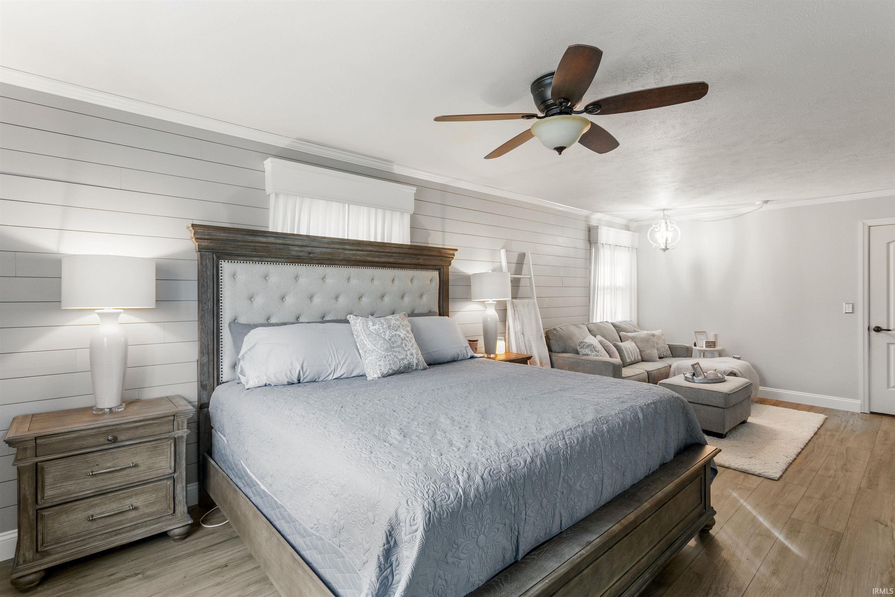 Bedroom featuring wood finished floors, a ceiling fan, wooden walls, and ornamental molding