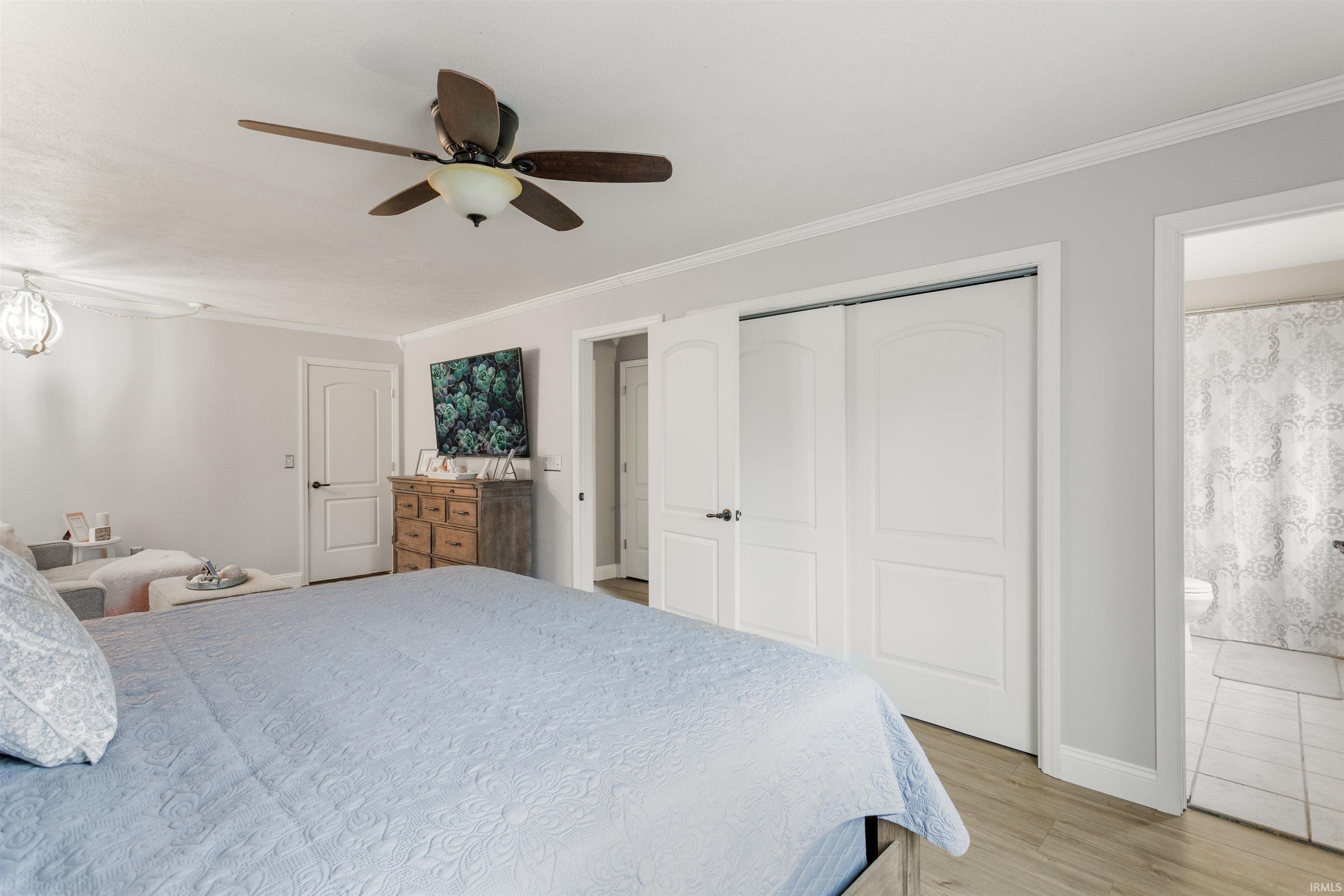 Bedroom featuring light wood finished floors, ceiling fan, a closet, ornamental molding, and ensuite bath