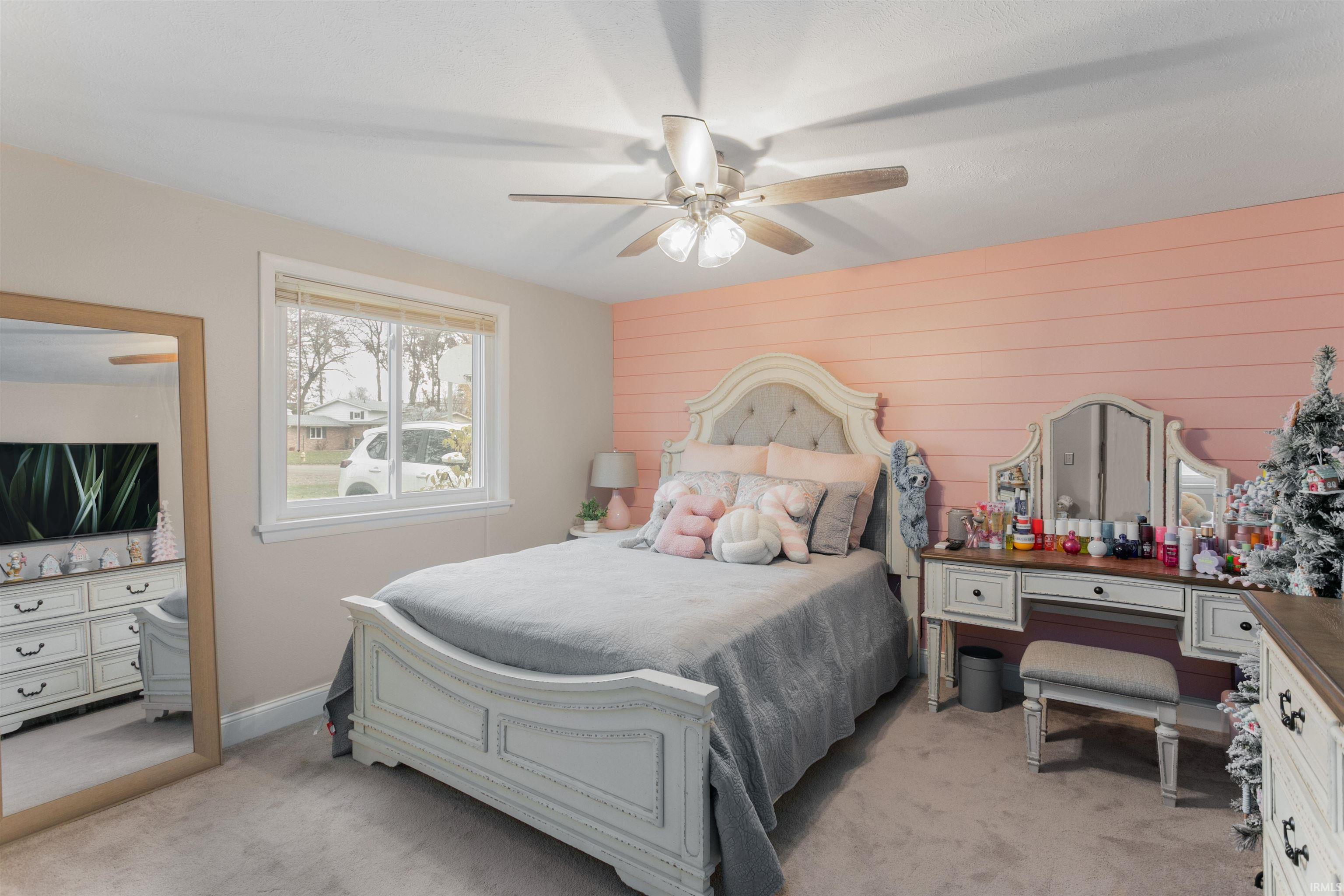 Bedroom featuring light colored carpet, wooden walls, and ceiling fan