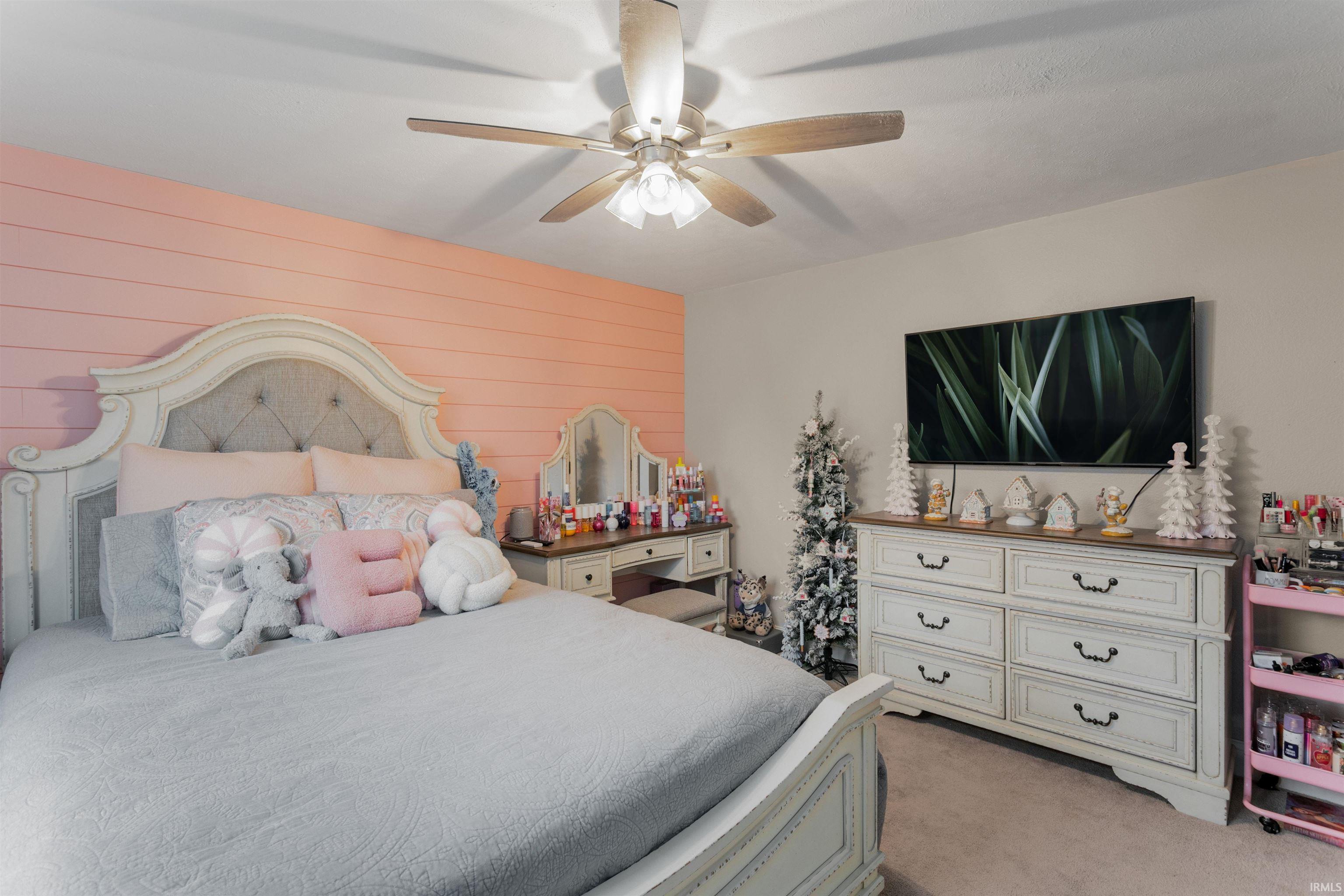 Bedroom with a ceiling fan, wooden walls, and light colored carpet