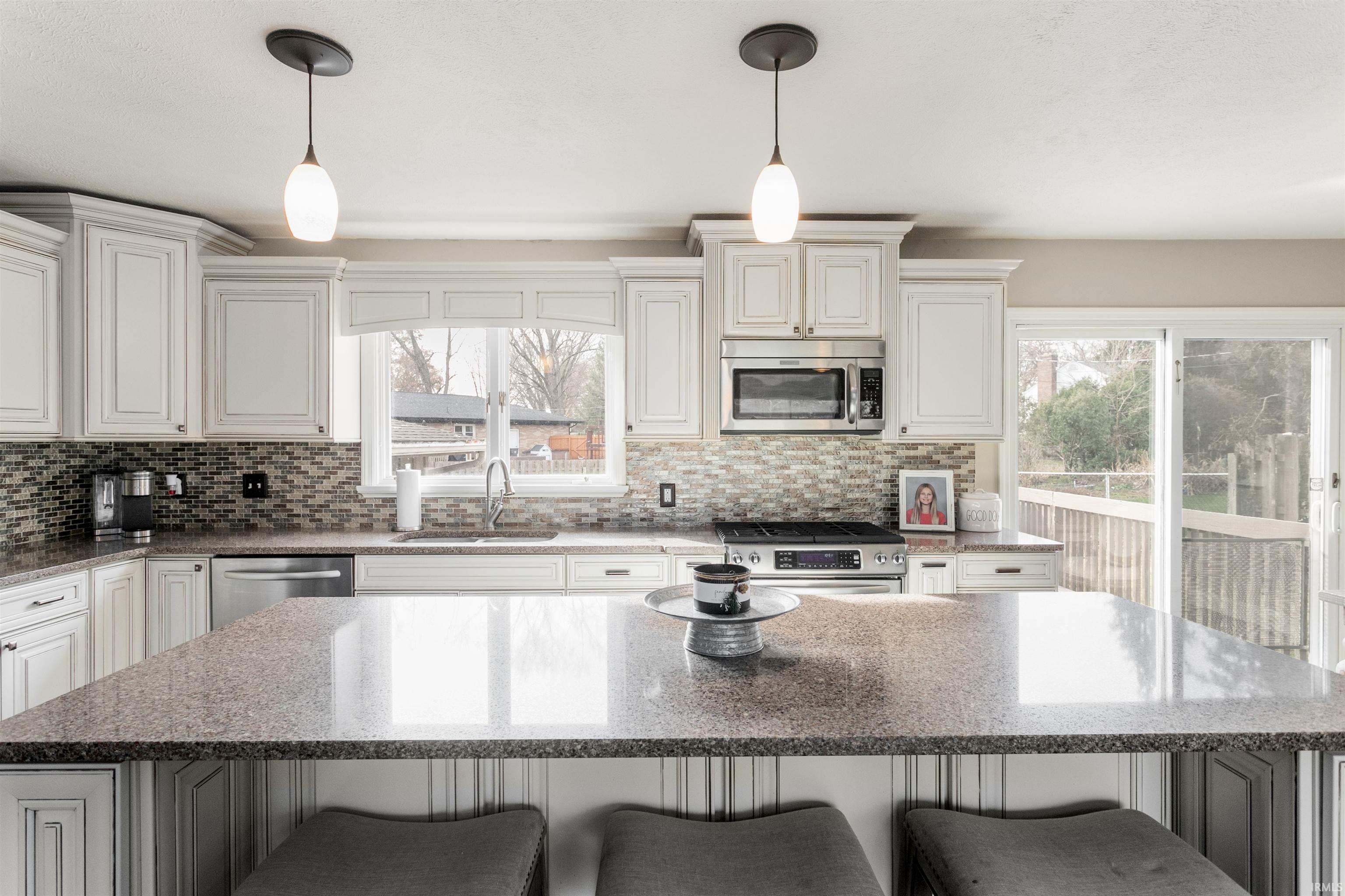 Kitchen with light stone countertops, a center island, appliances with stainless steel finishes, and pendant lighting