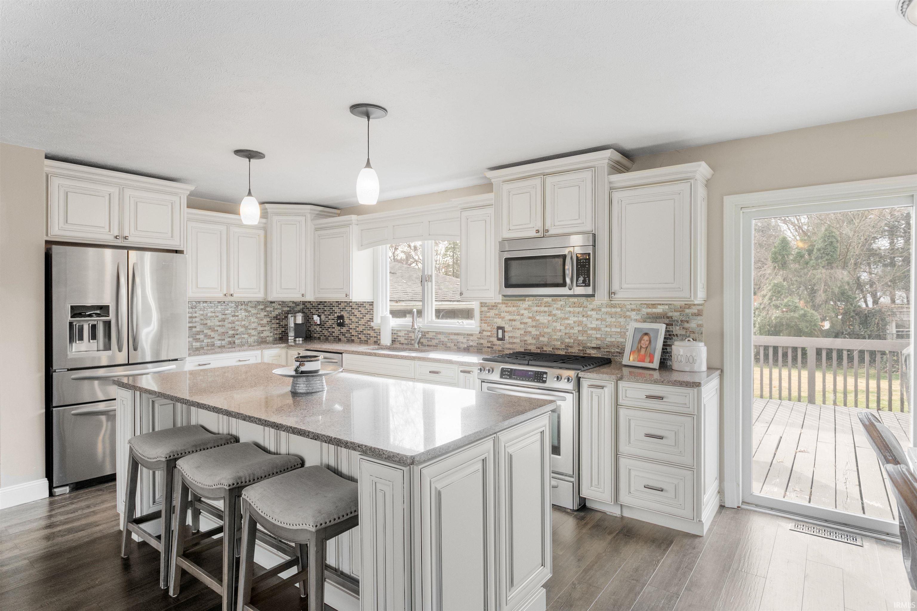 Kitchen featuring appliances with stainless steel finishes, decorative light fixtures, light stone counters, a breakfast bar area, and a center island