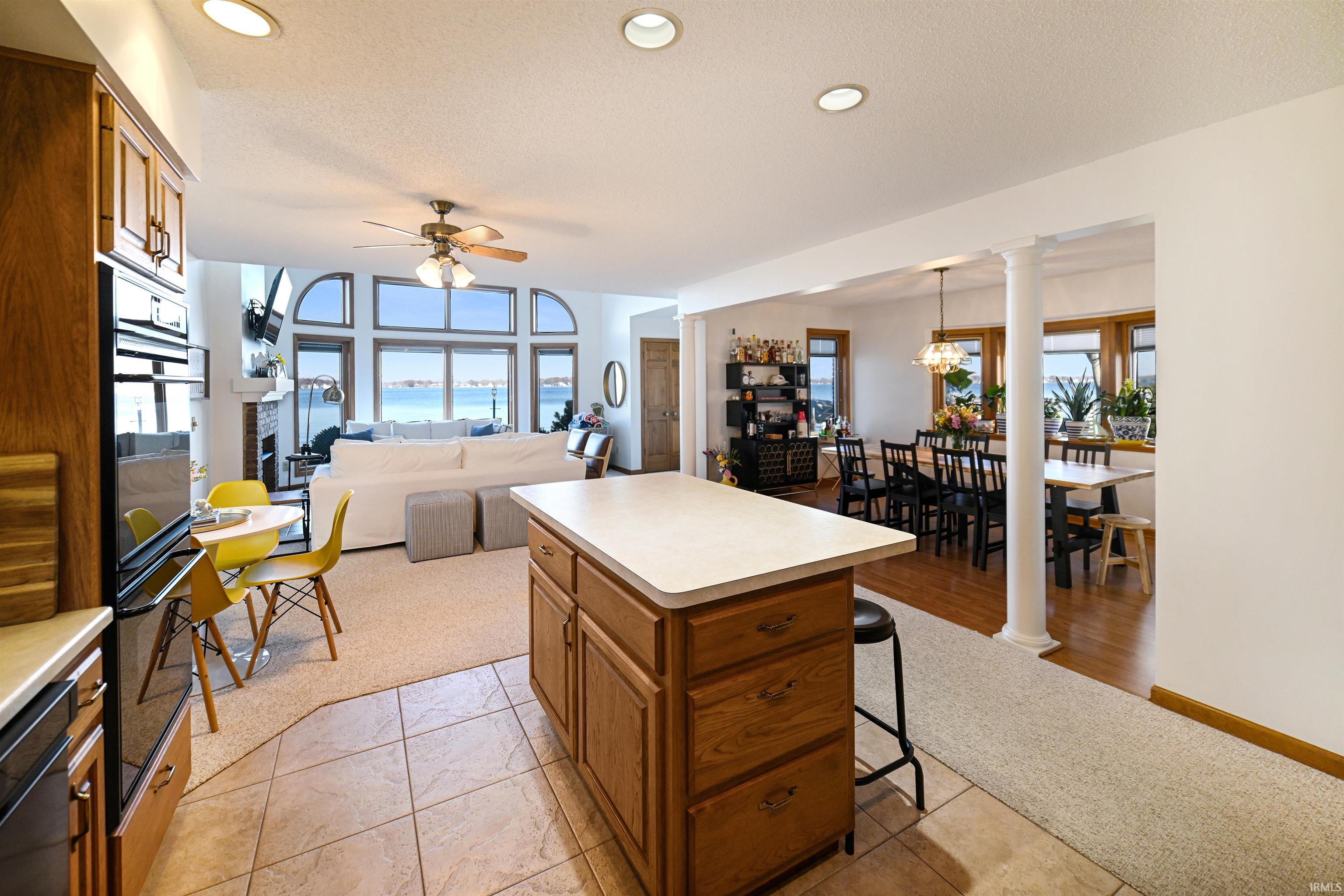 Kitchen with ornate columns, a textured ceiling, brown cabinetry, light countertops, and light carpet